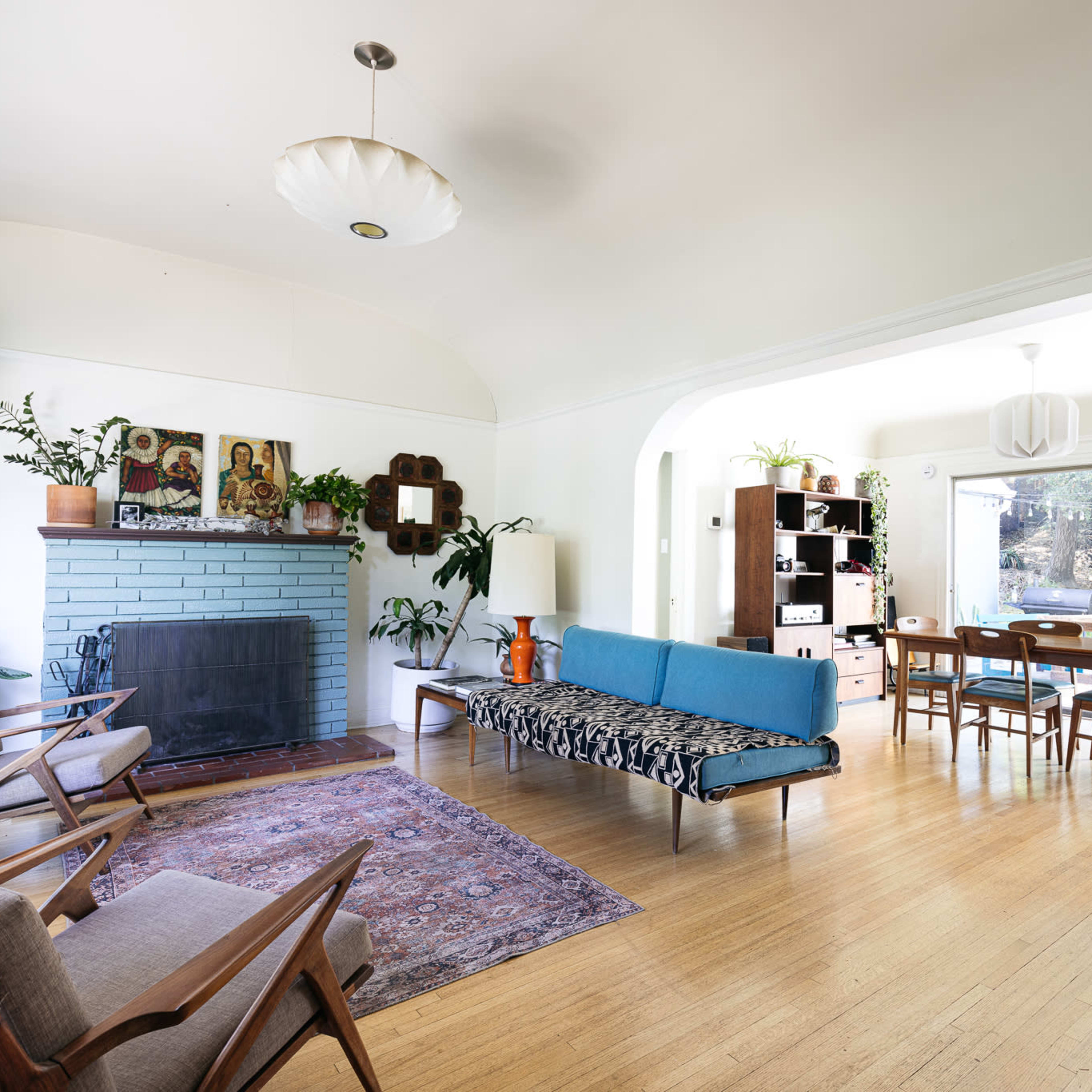 A modern living room with a blue sofa, wooden chairs, a fireplace, and a dining area visible through an archway.