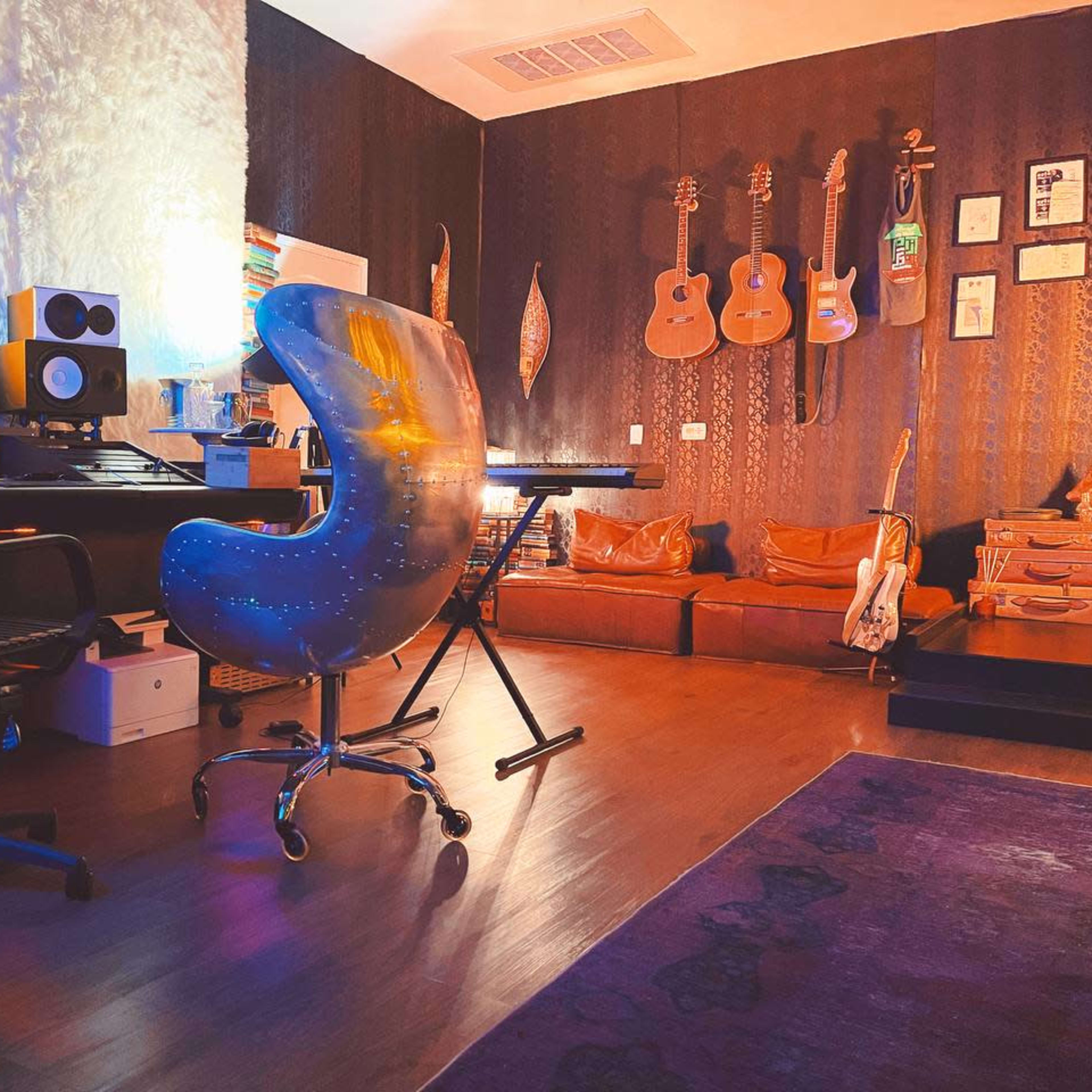A music studio with a desk, an ergonomic chair, and various guitars hanging on the wall.