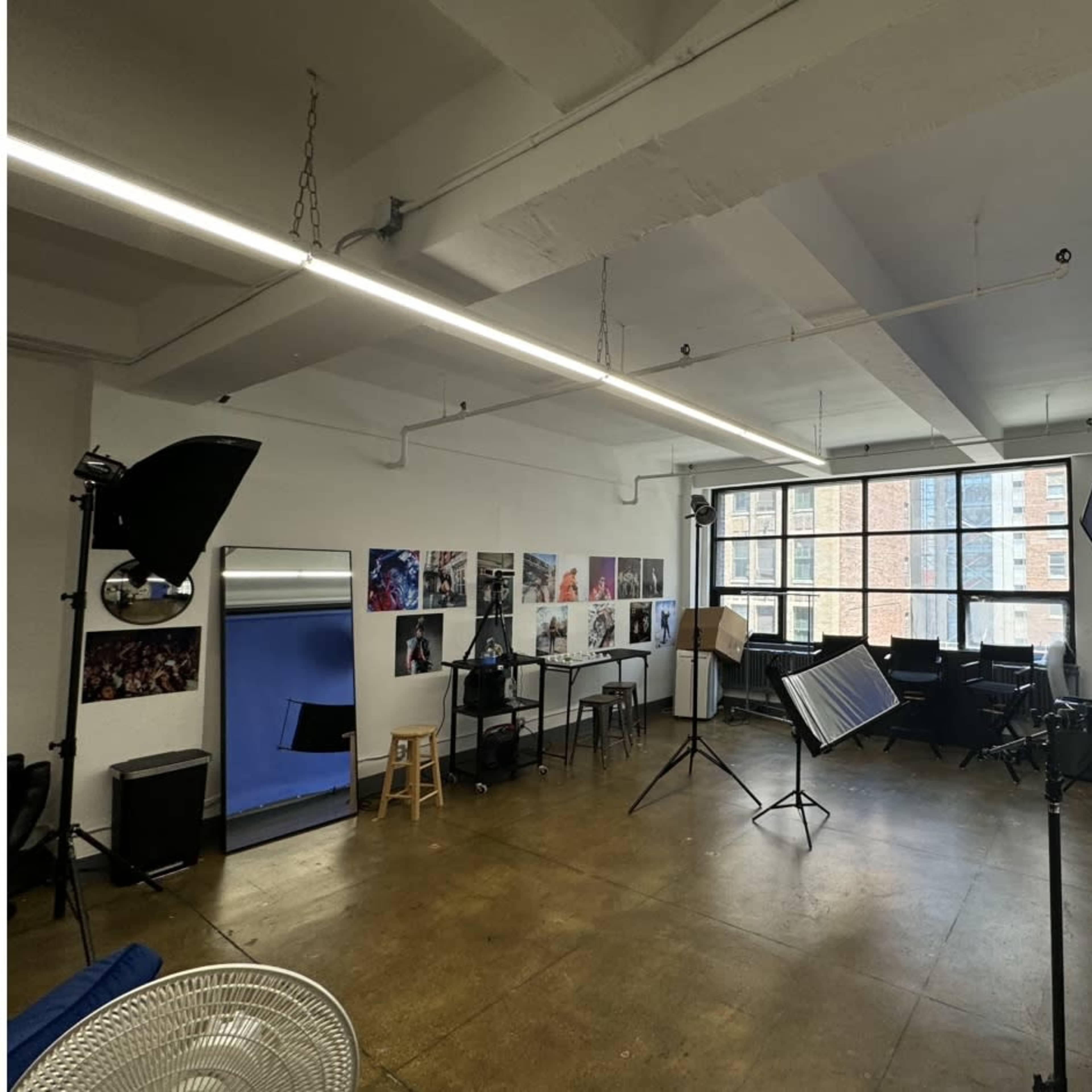 A photography studio with a blue backdrop, various lighting equipment, and several photo displays on the walls.