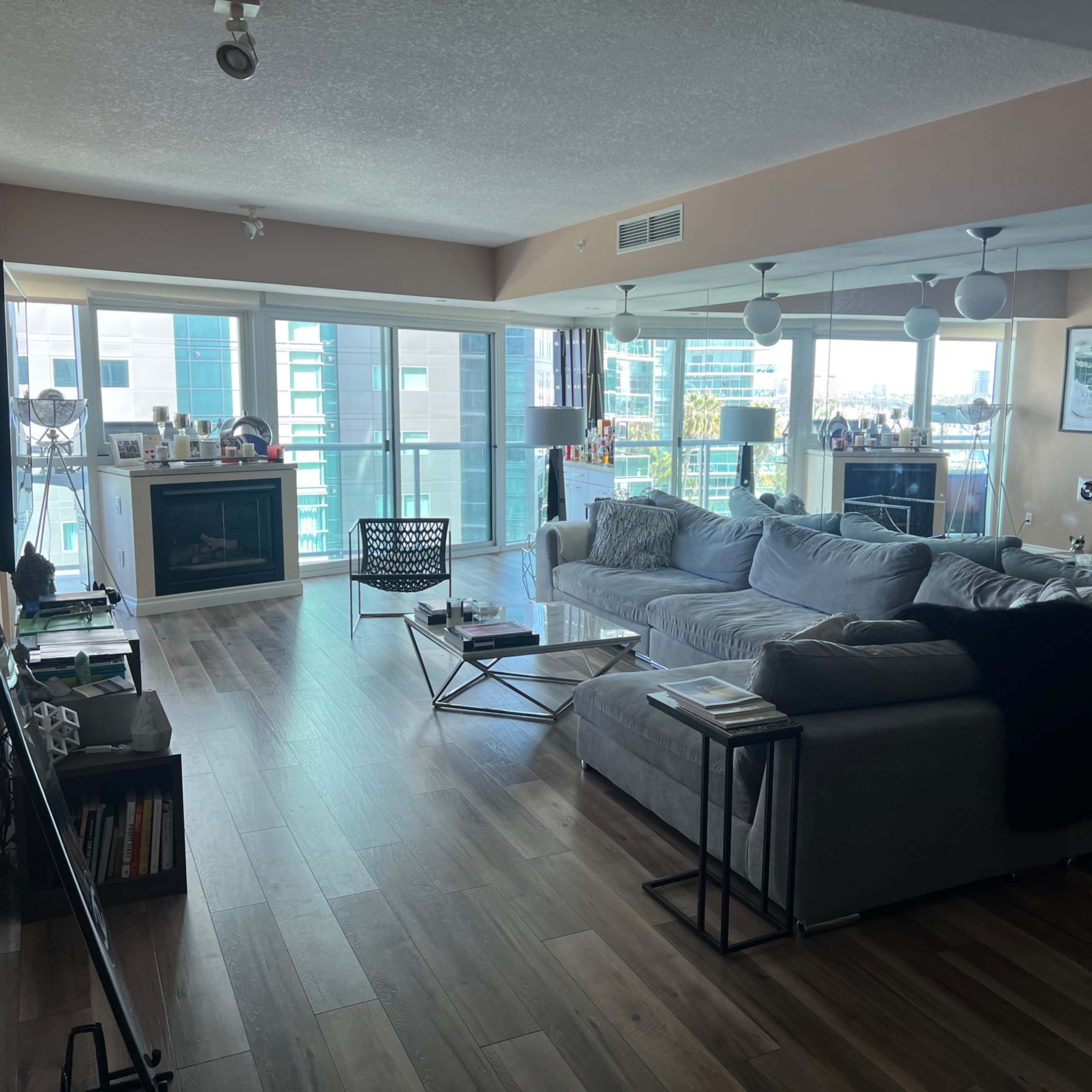 A modern living room with large windows, a sectional sofa, a glass coffee table, and a TV mounted on the wall.