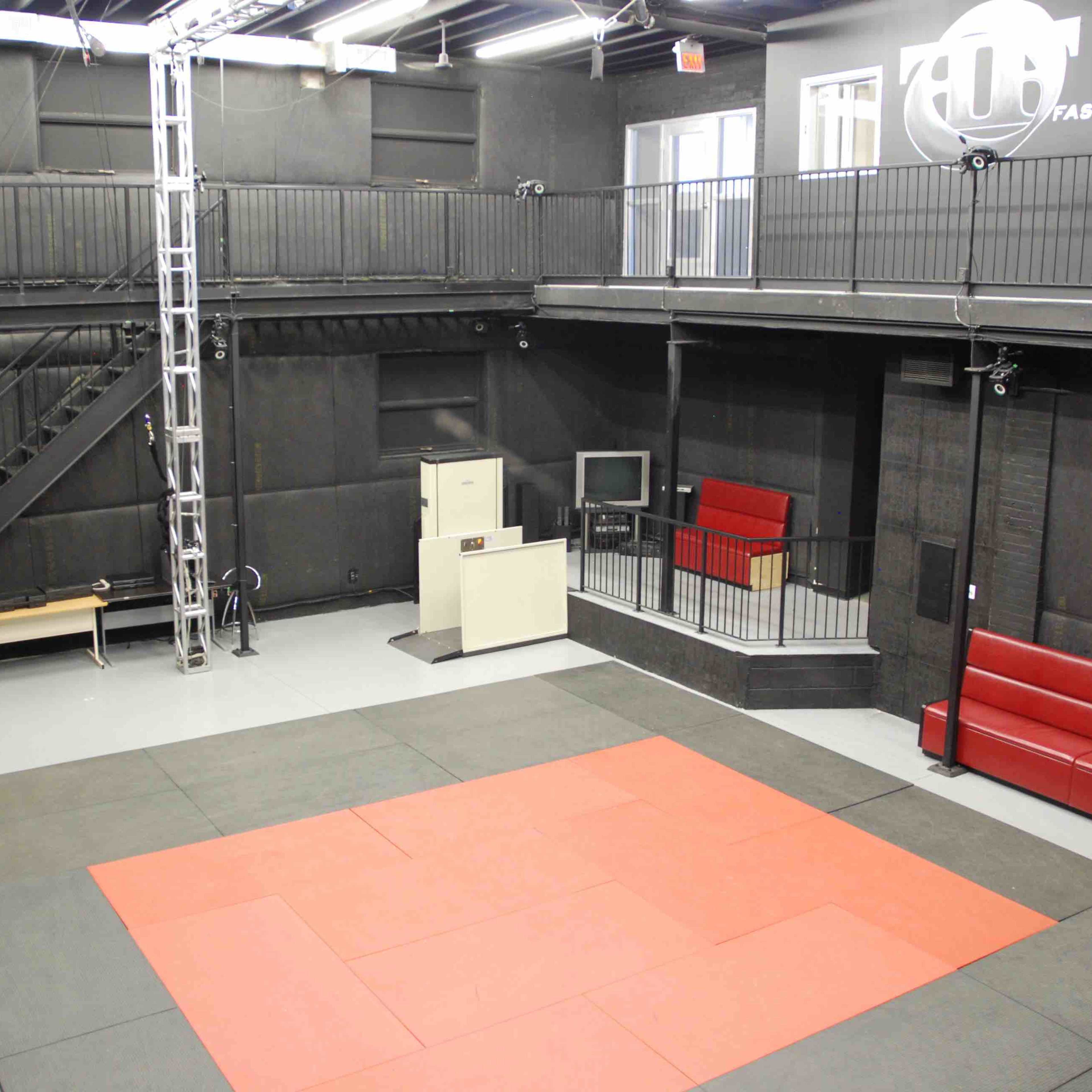 A spacious gym or studio with a padded training area, a staircase, and seating along the walls.