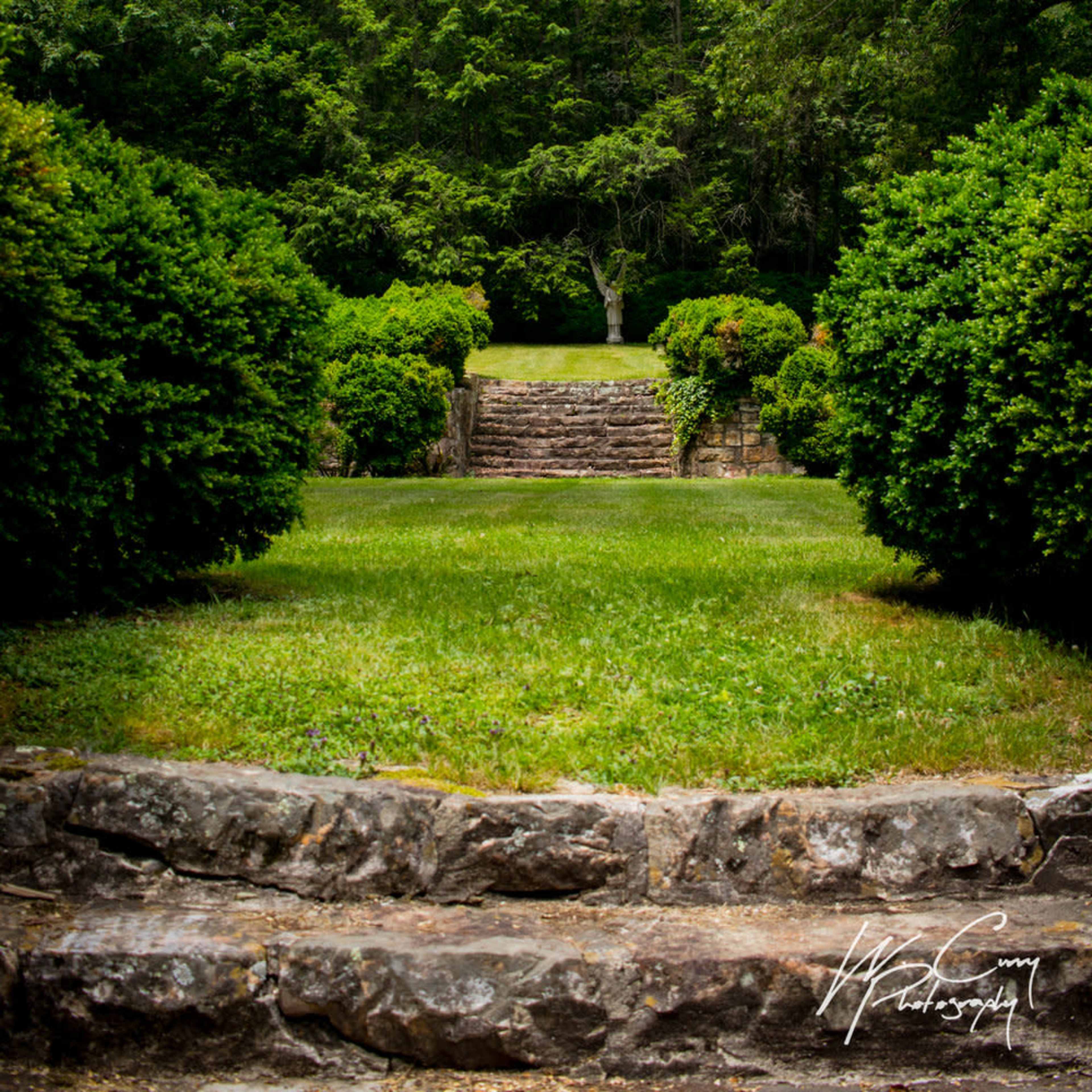 A stone staircase leading up to a grassy area surrounded by shrubbery and trees.