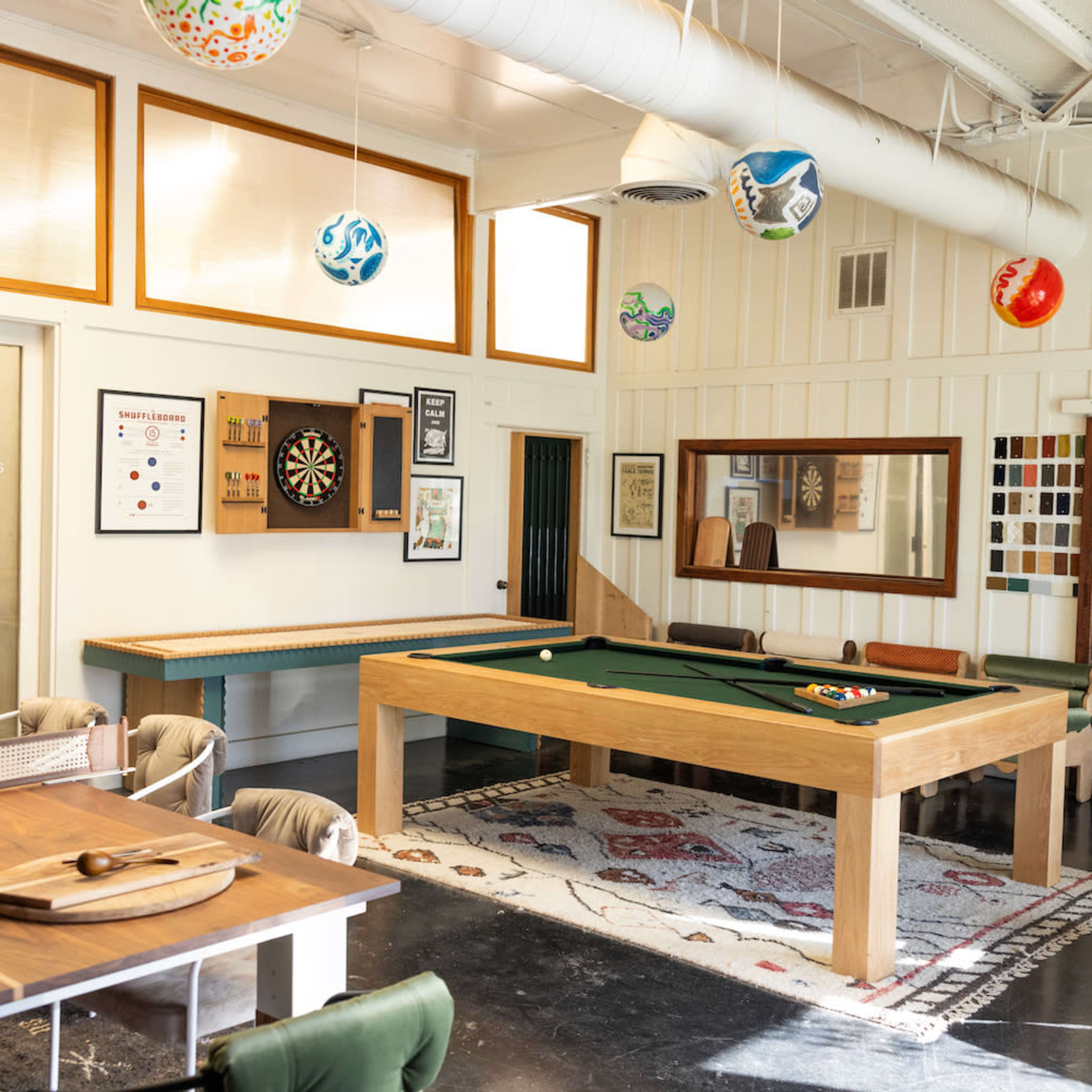 A recreational room featuring a pool table, dartboard, and various decorative elements on the walls, with a mix of seating arrangements and a large mirror.