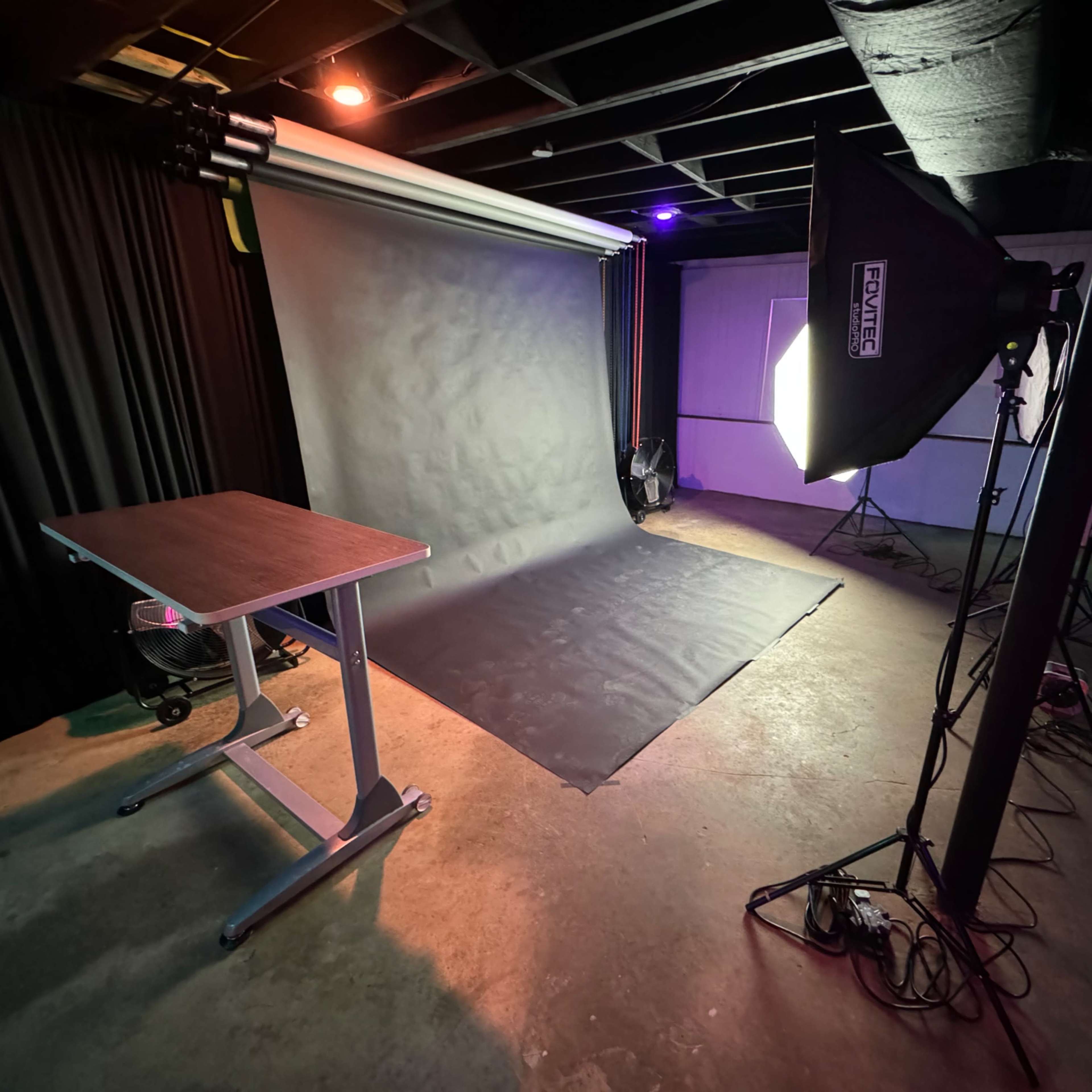 A photography studio setup featuring a backdrop, a table, and lighting equipment arranged on a concrete floor.