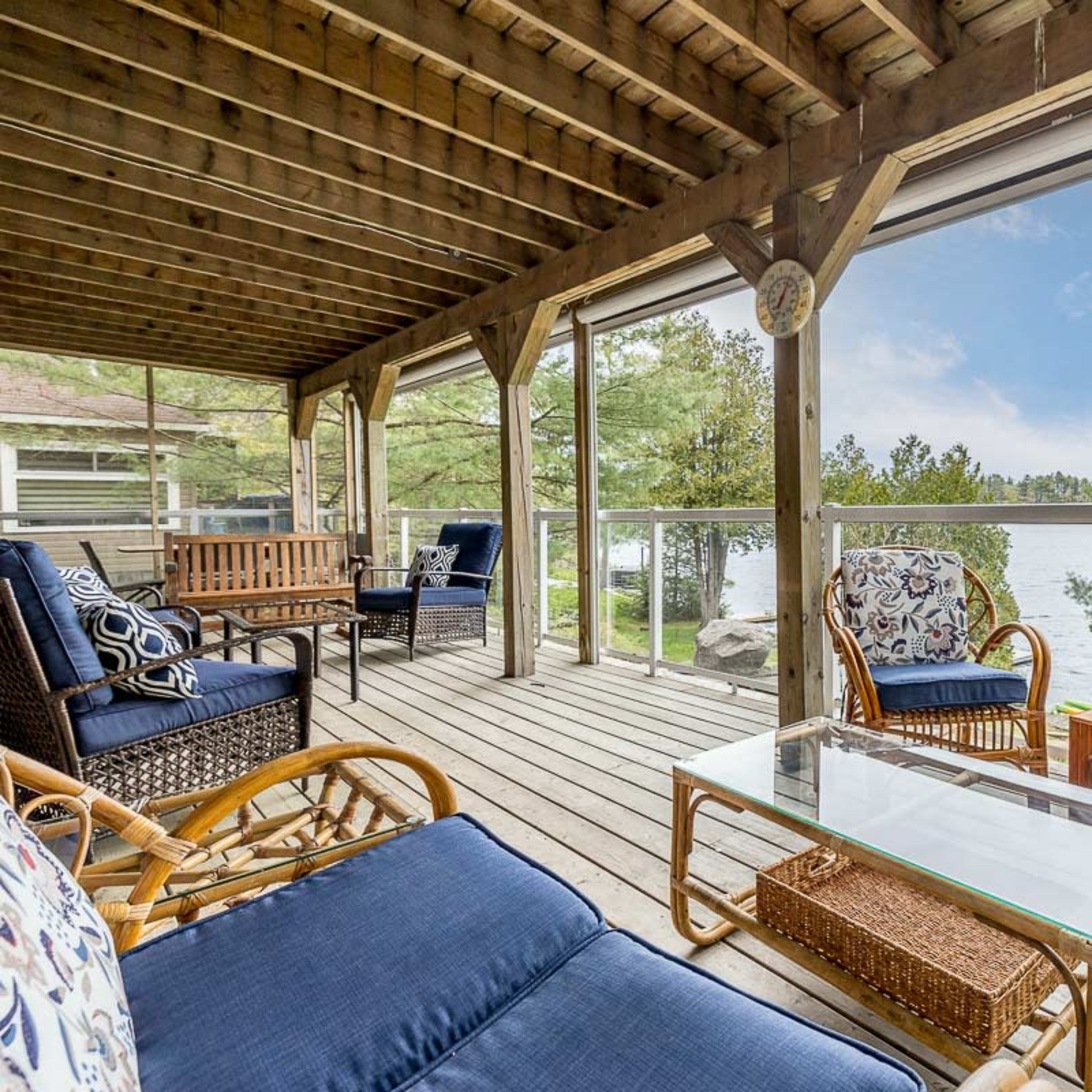 A wooden deck overlooking a lake, furnished with blue cushioned seating and a glass-topped coffee table.