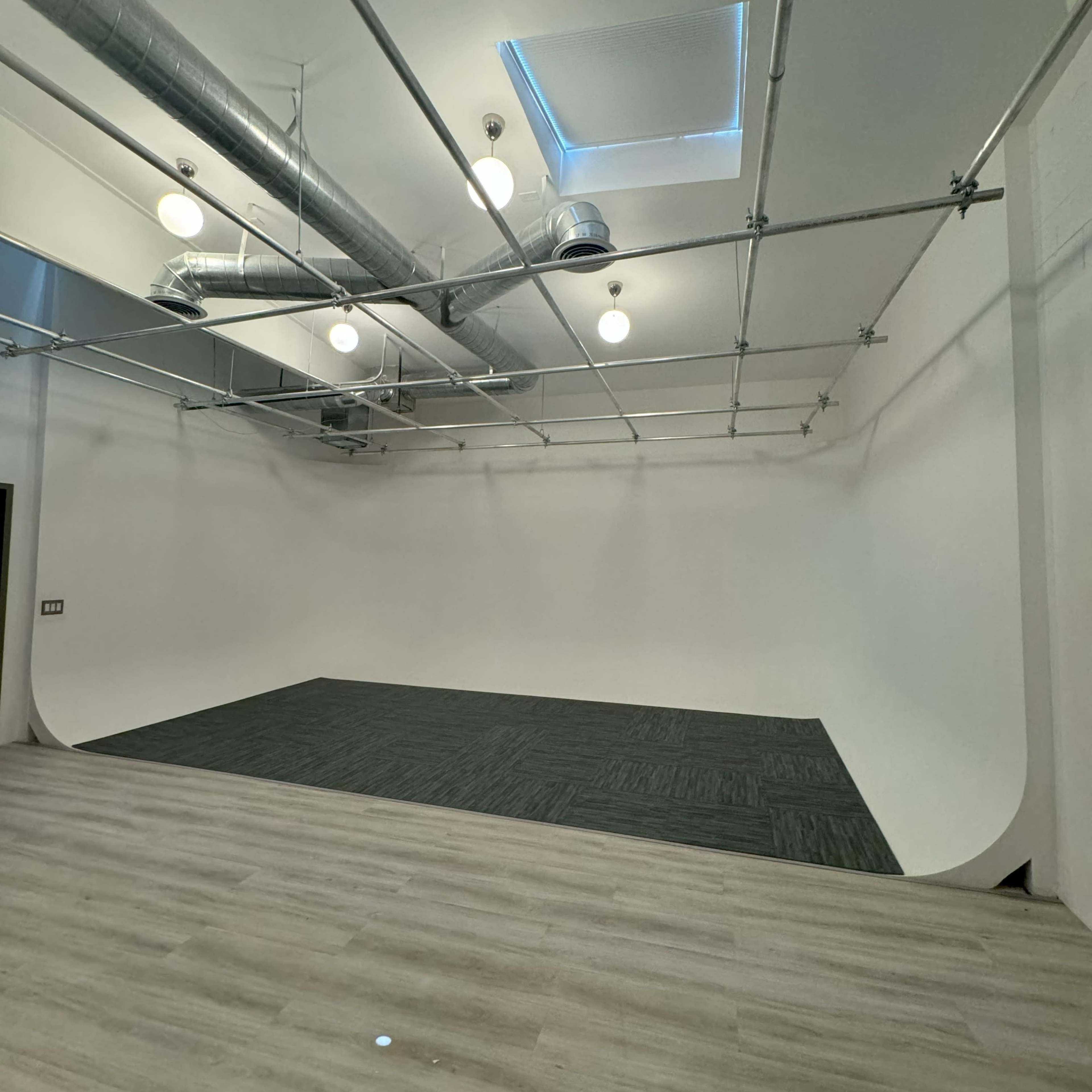 An empty studio space with a seamless white backdrop, gray flooring, and overhead lighting fixtures.