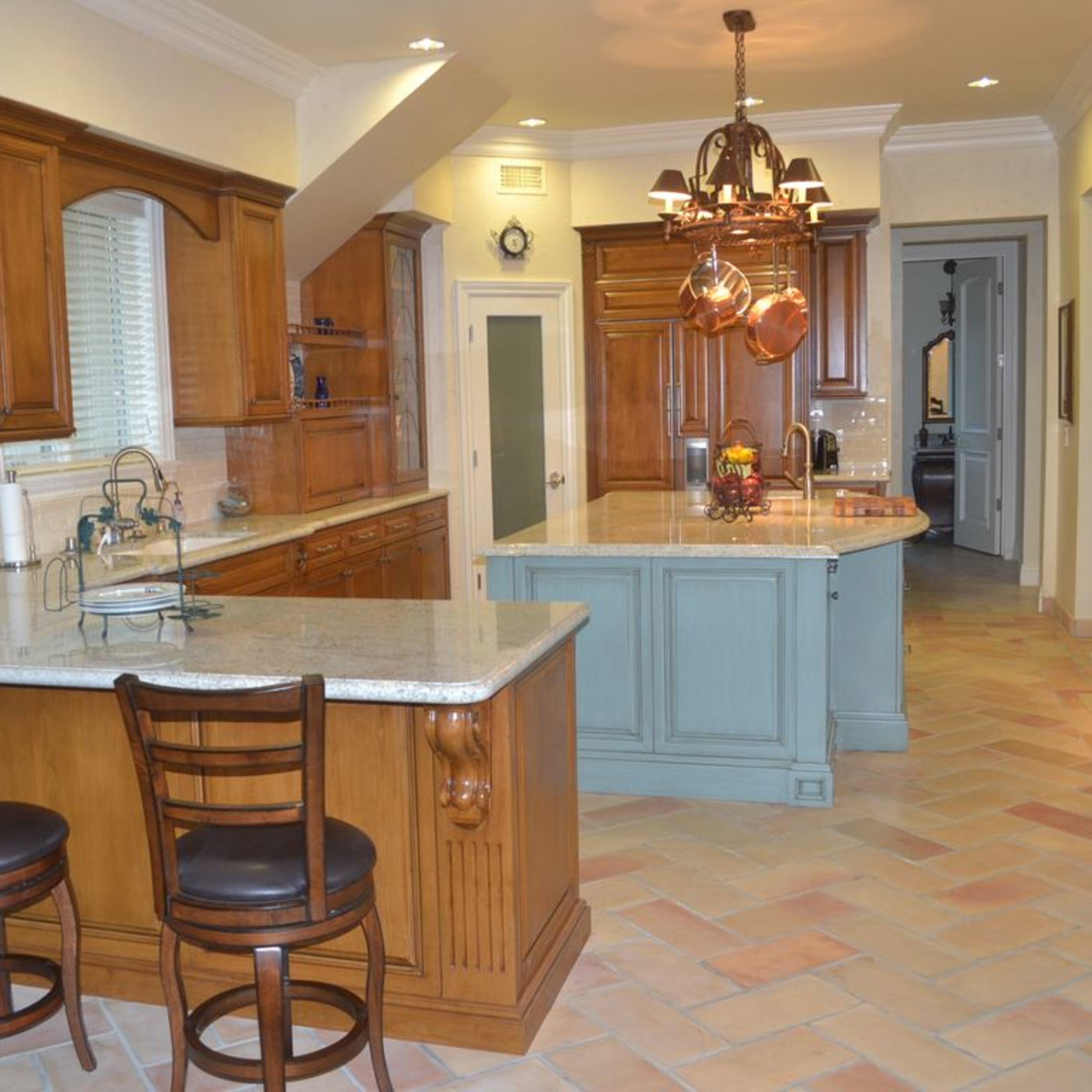 A spacious kitchen featuring wooden cabinetry, a central island with a light blue finish, and a set of three bar stools.