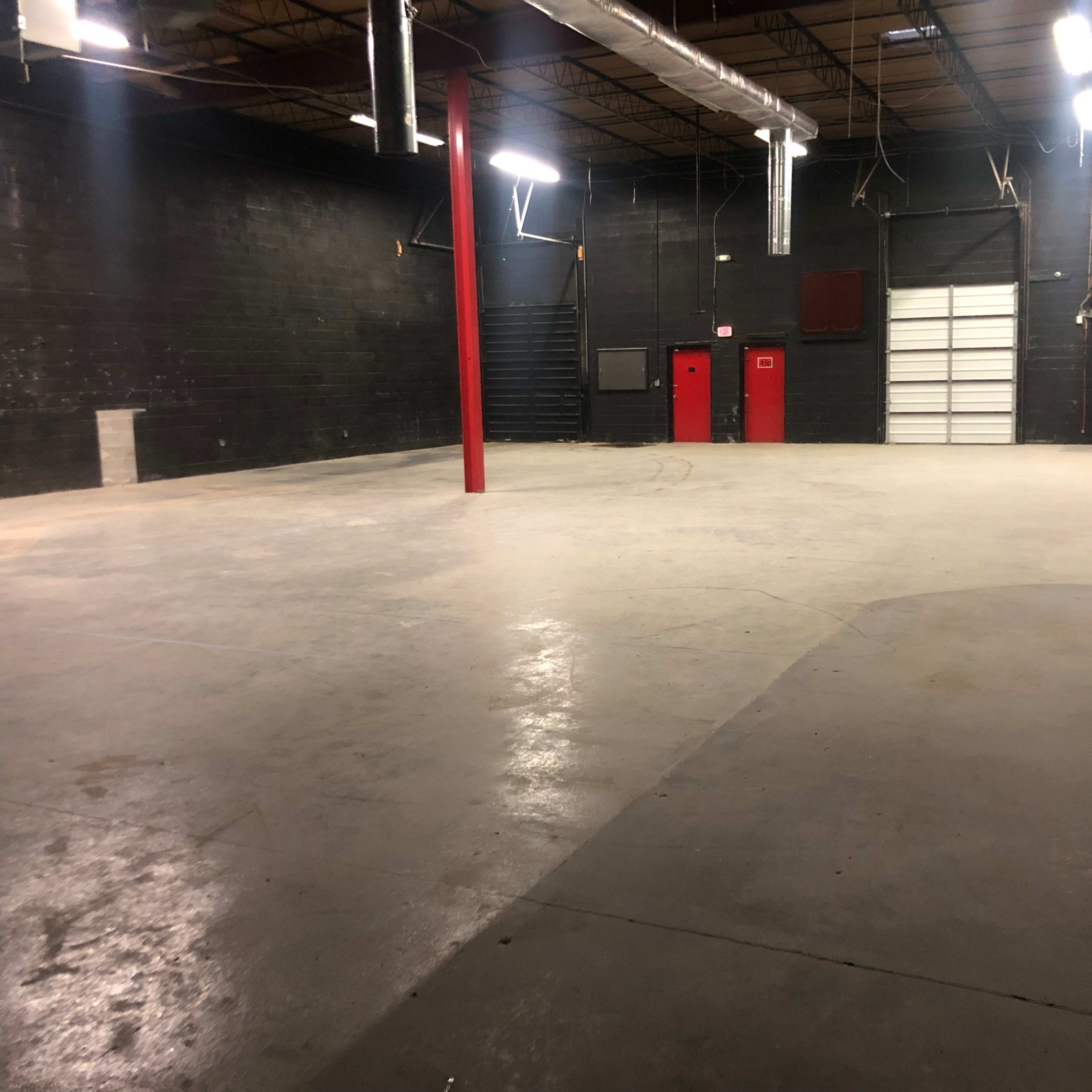 An empty industrial warehouse space with a concrete floor and black-painted walls.