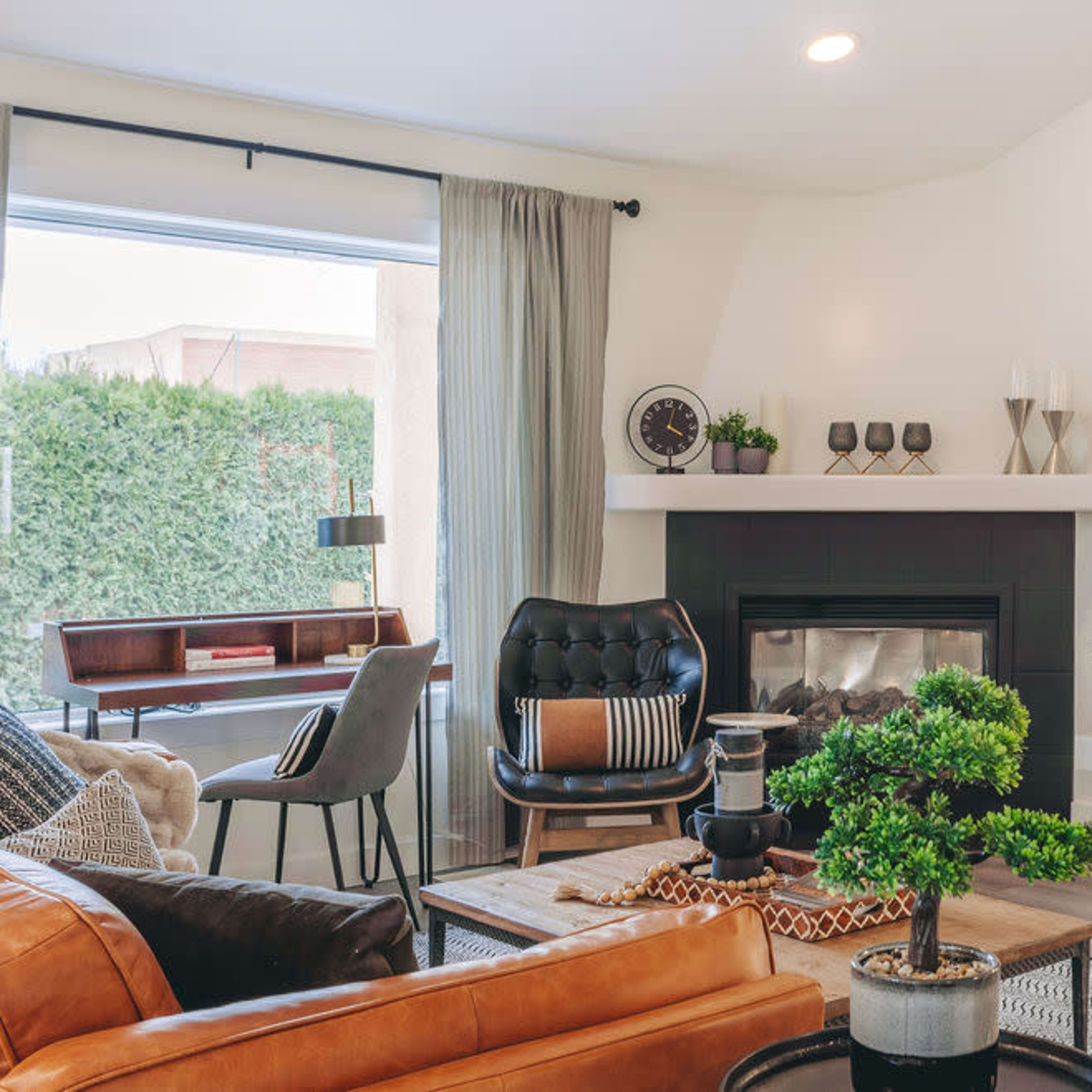 A modern living room featuring a fireplace, a television mounted on the wall, and a mix of seating options including a leather sofa and a black armchair, with a window providing natural light.