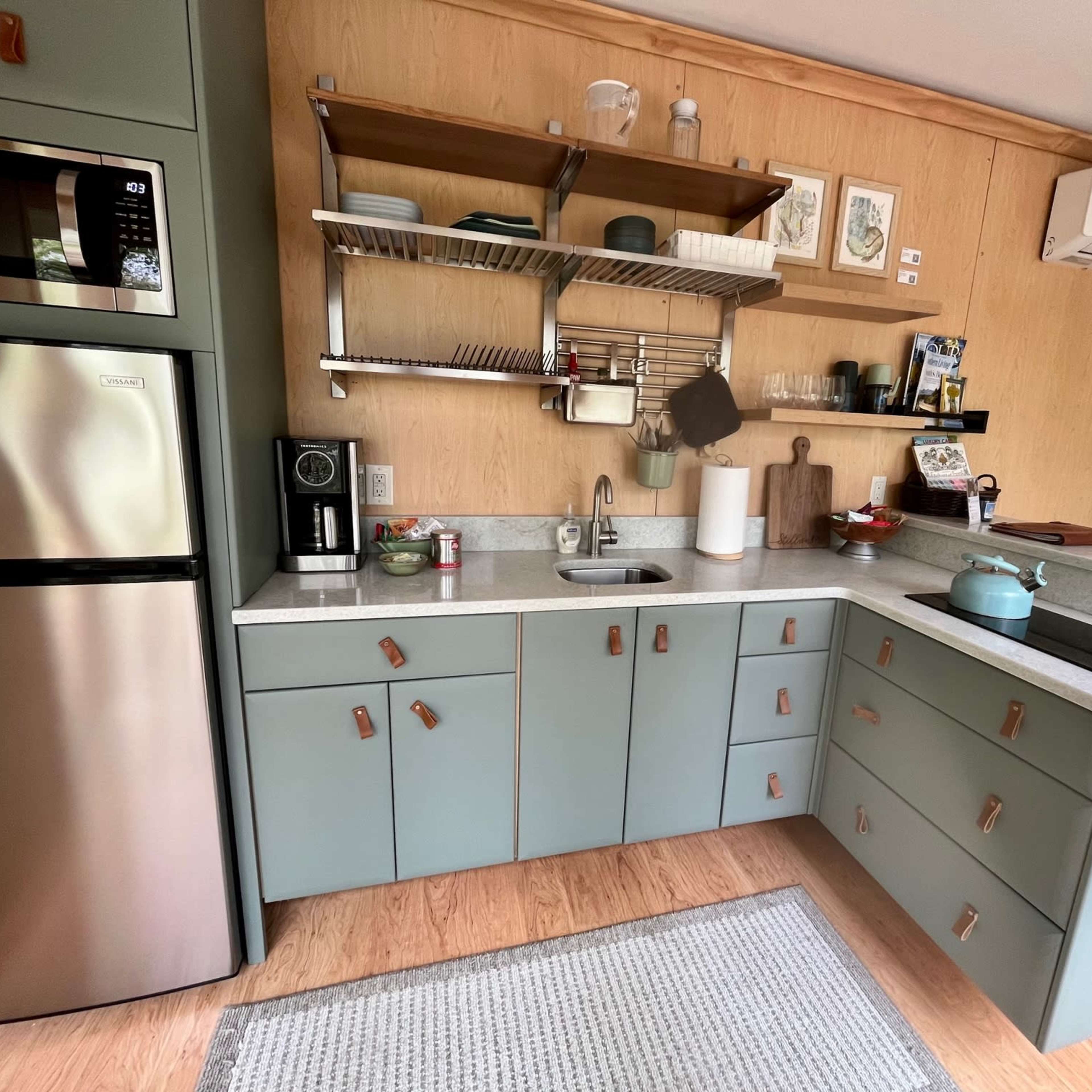 A modern kitchen features mint green cabinetry, stainless steel appliances, and a wooden accent wall, with open shelving displaying various kitchenware.