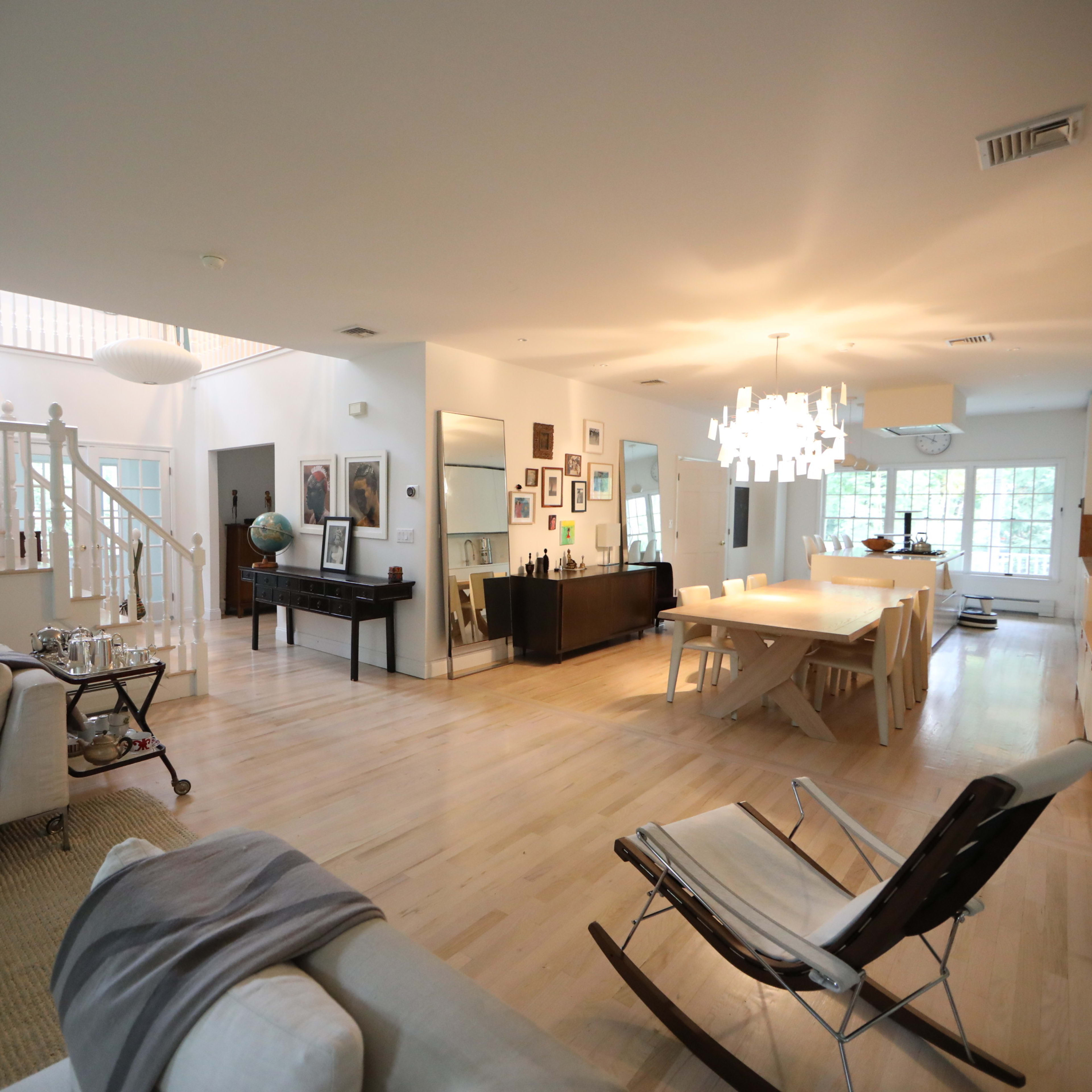 A spacious, open-concept living area connected to a dining space, featuring light wood flooring and modern furnishings.