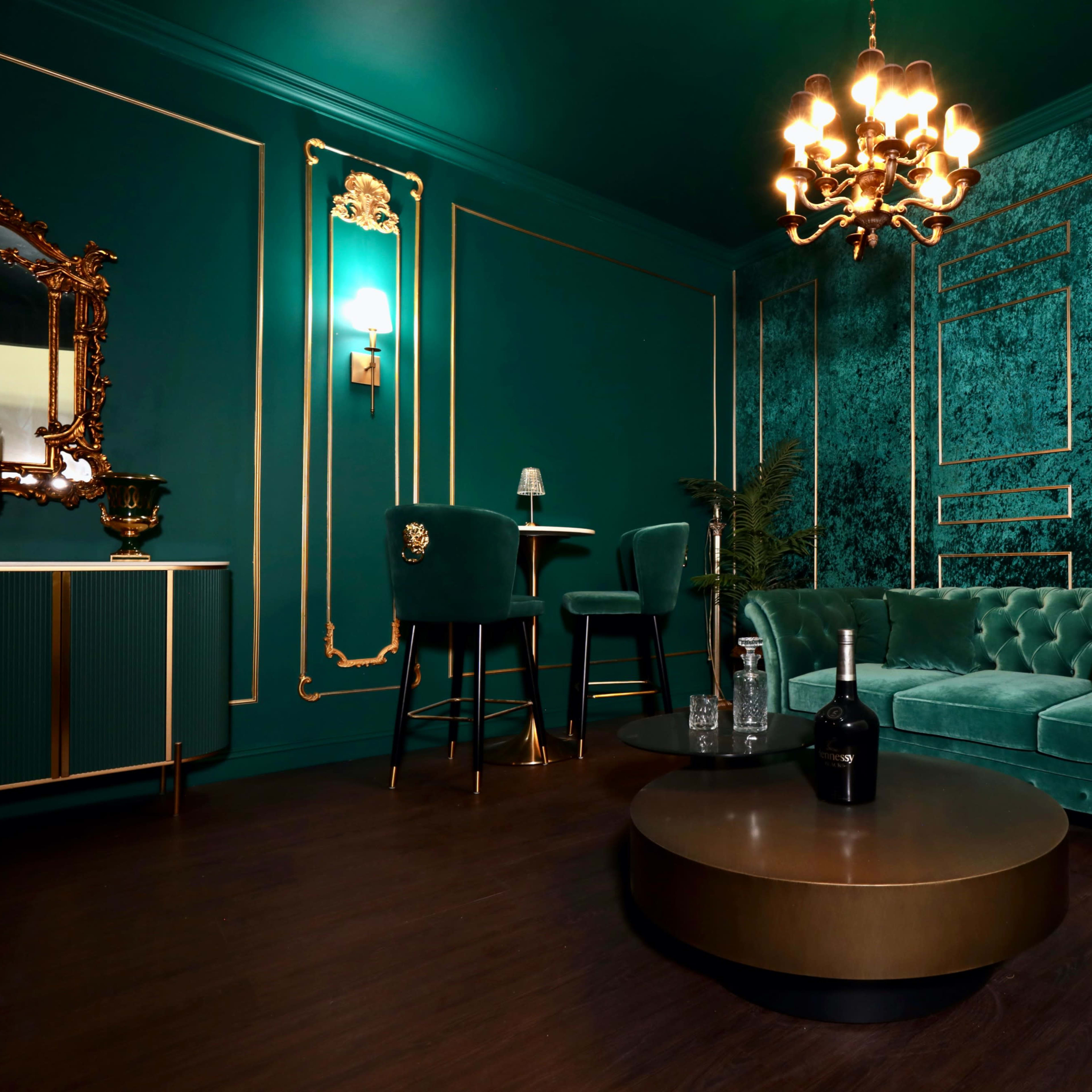 An elegant room with teal walls, a plush velvet sofa, a round coffee table, and a chandelier.