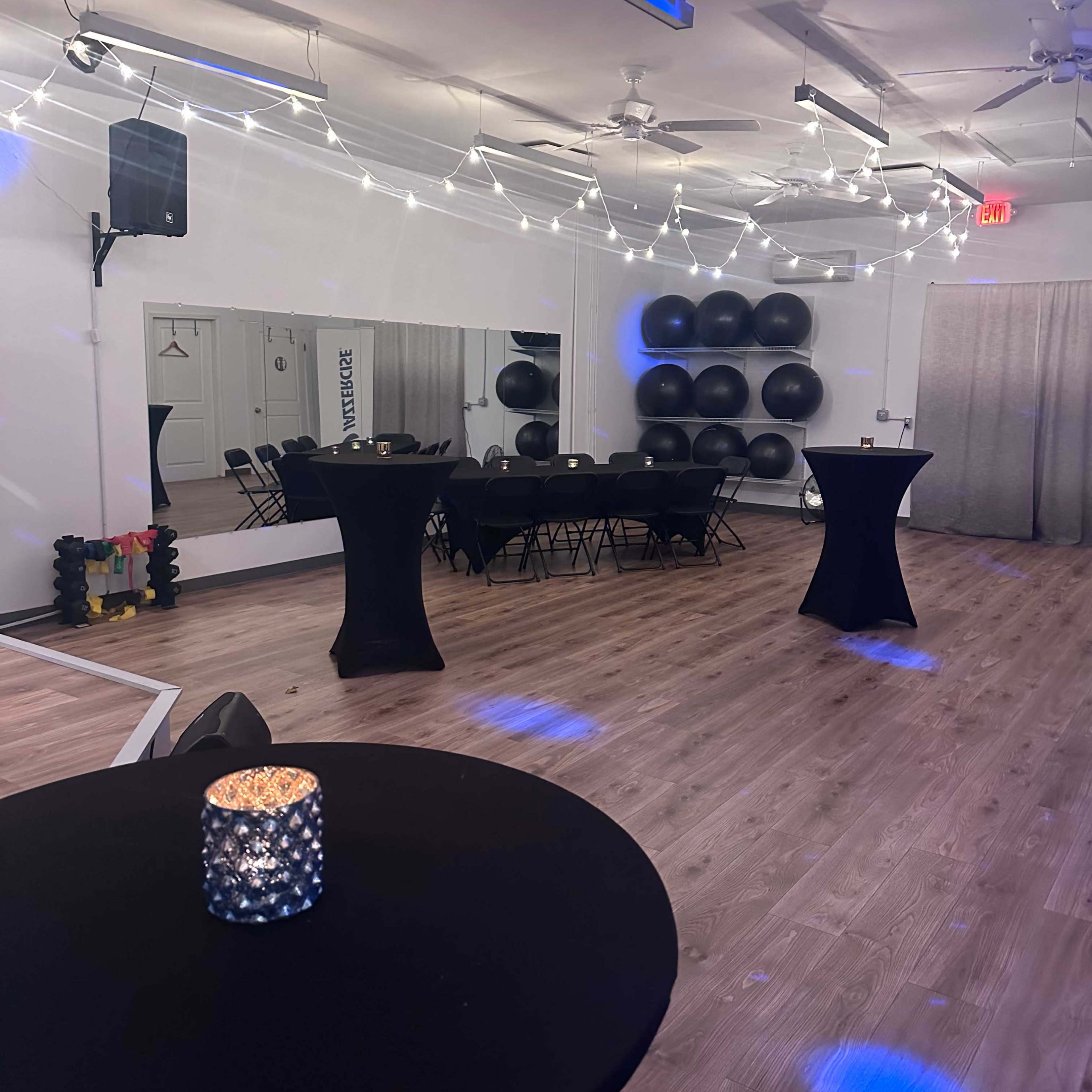 The room features black tables, string lights overhead, and exercise balls arranged against a wall.