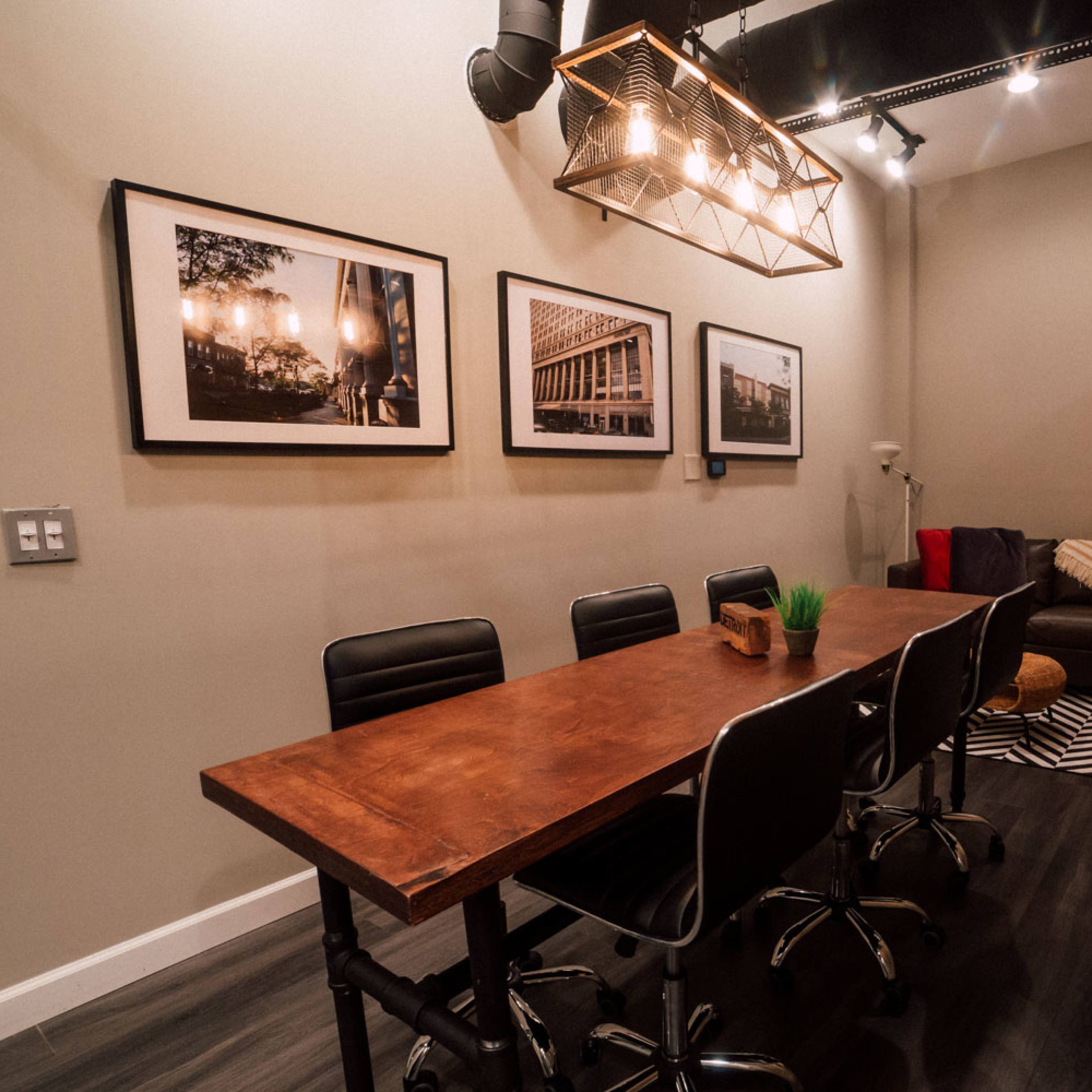 A modern meeting room with a wooden table surrounded by black chairs, framed photographs on the walls, and a cozy seating area in the corner.