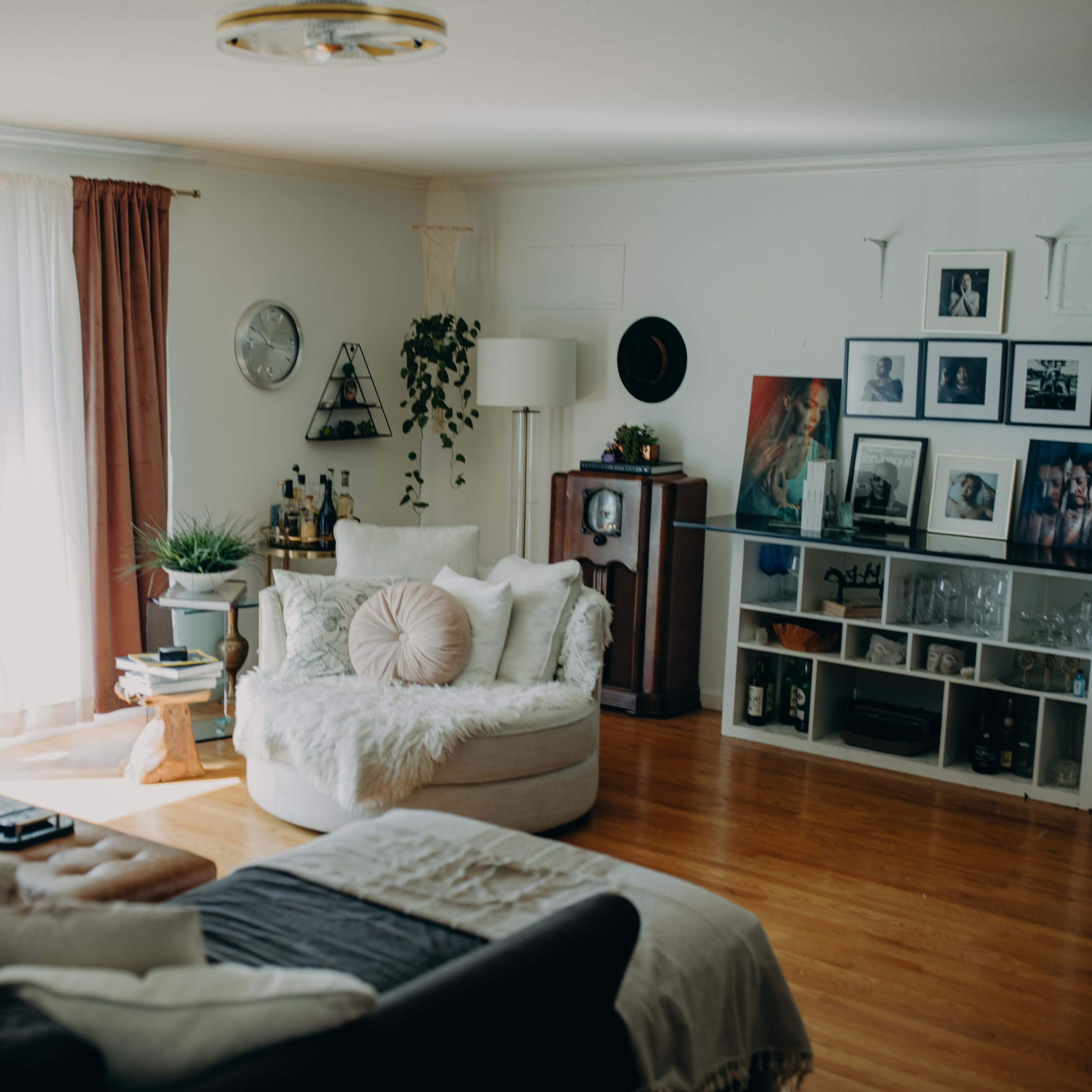 The living room features a cozy seating area with a large circular chair, a dark sofa, and various plants, along with a mix of framed artwork on the walls.