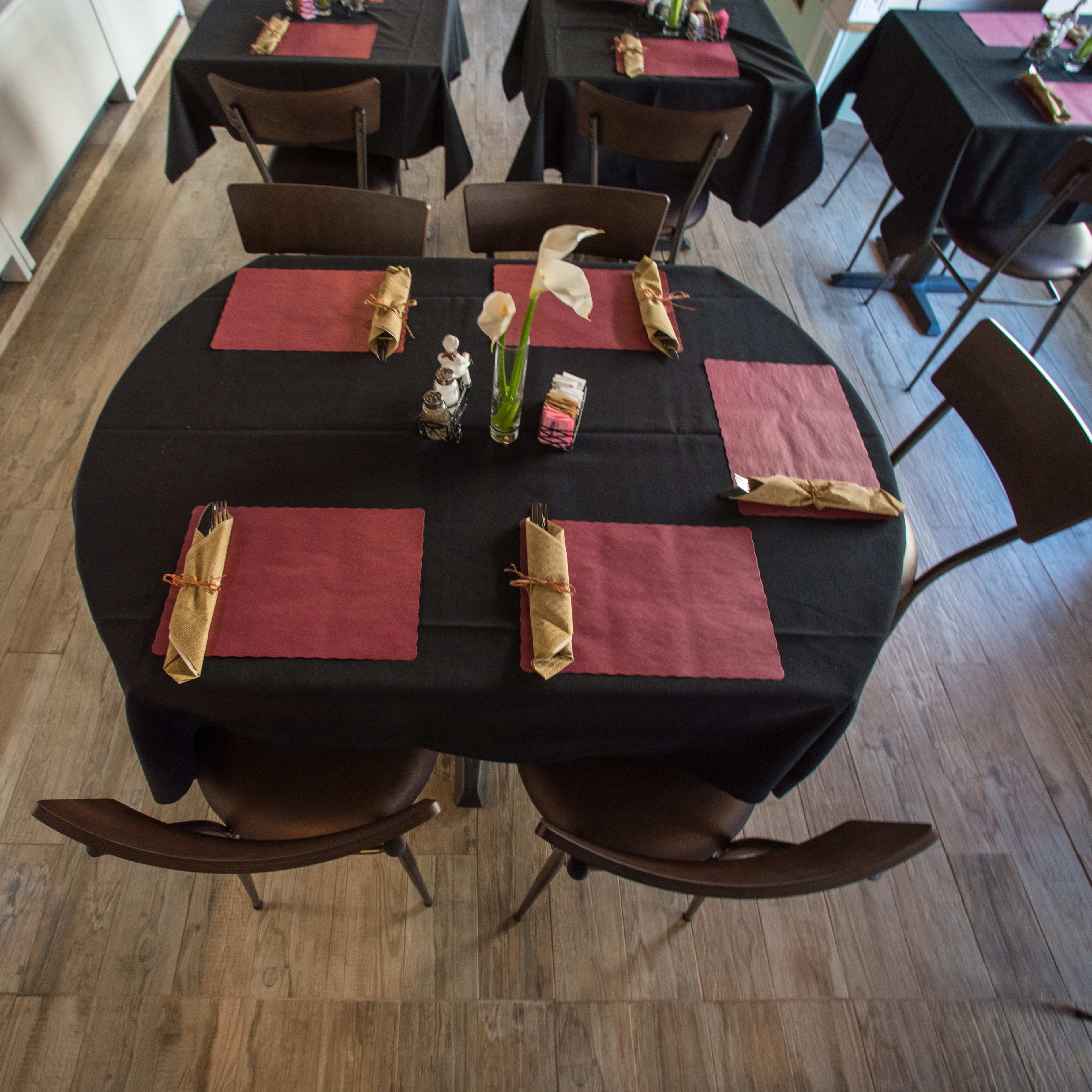 A restaurant setting with black tables covered in black tablecloths, each adorned with maroon placemats and decorative napkin folds.
