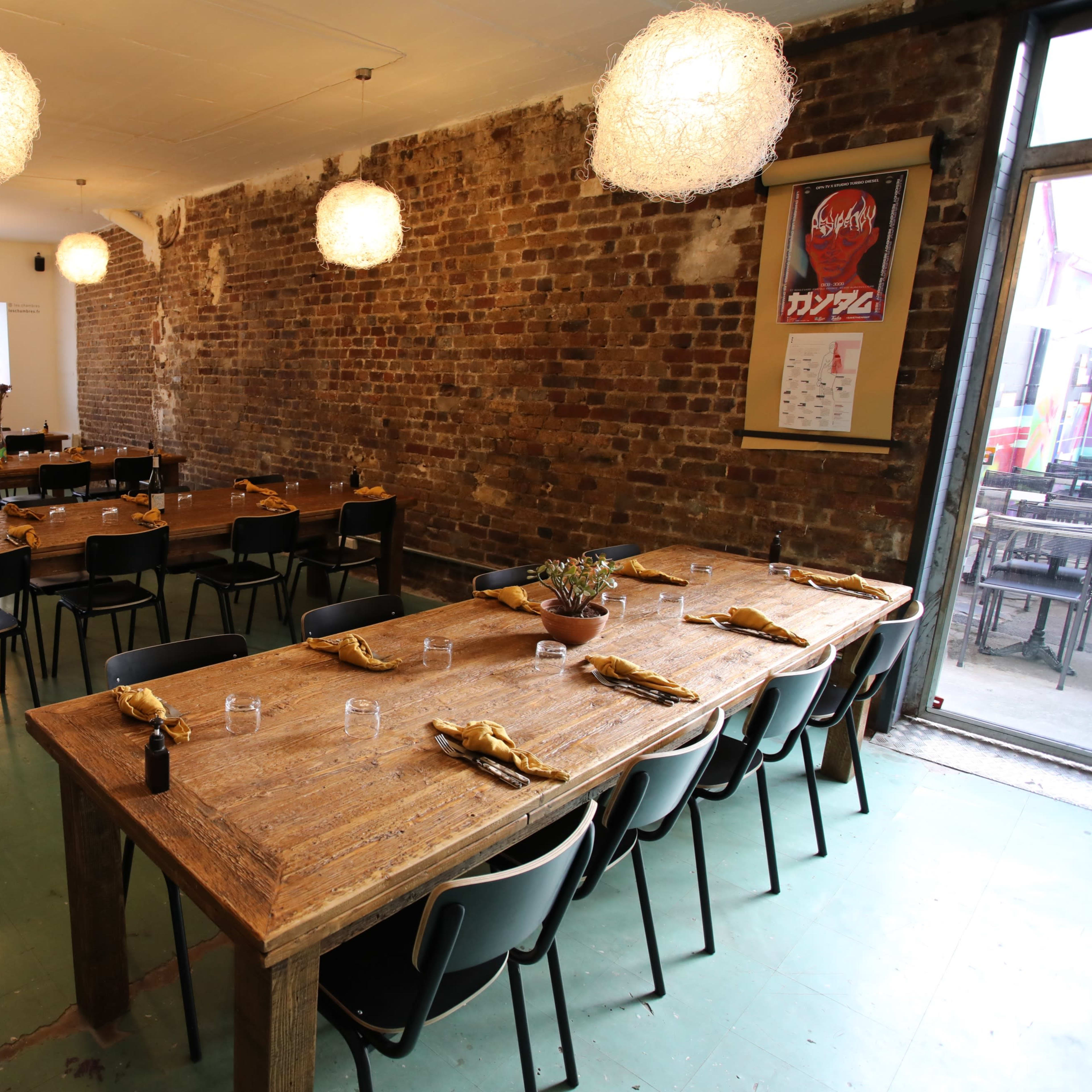 A spacious restaurant with wooden tables set for dining, exposed brick walls, and pendant lighting.