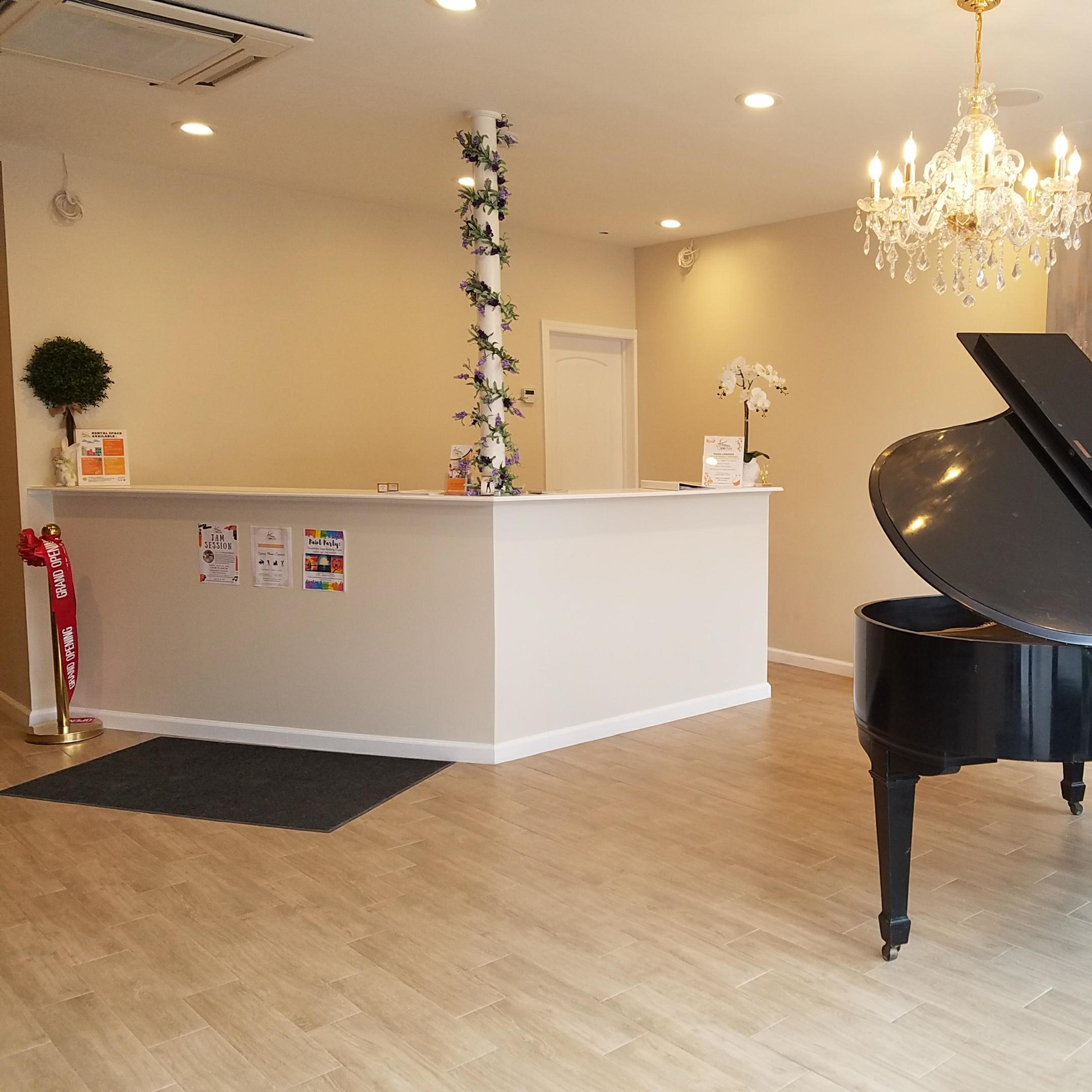 A reception area featuring a black grand piano, a chandelier, and a minimalist counter with floral decorations.