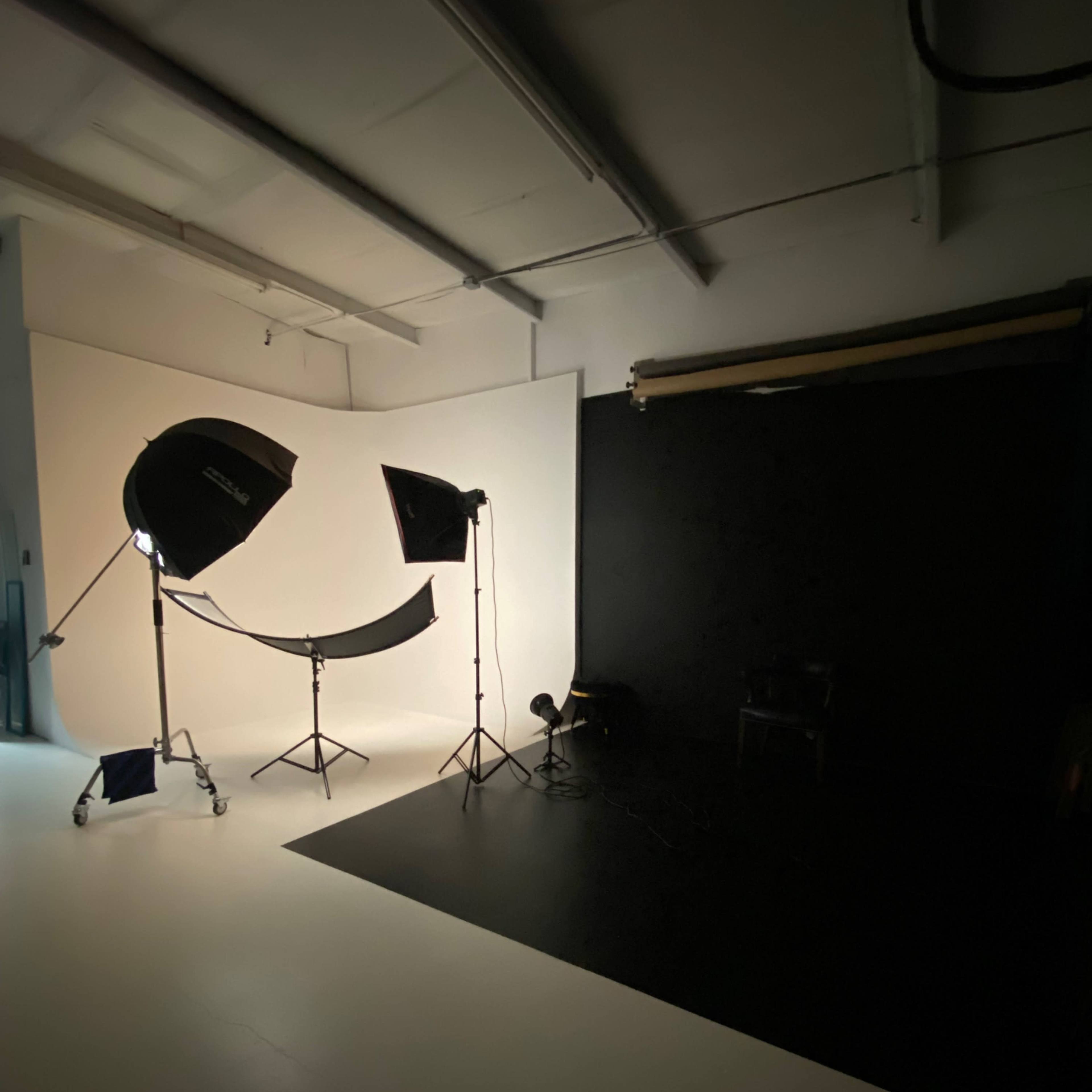 A photography studio with lighting equipment set up against a backdrop of white and black surfaces.