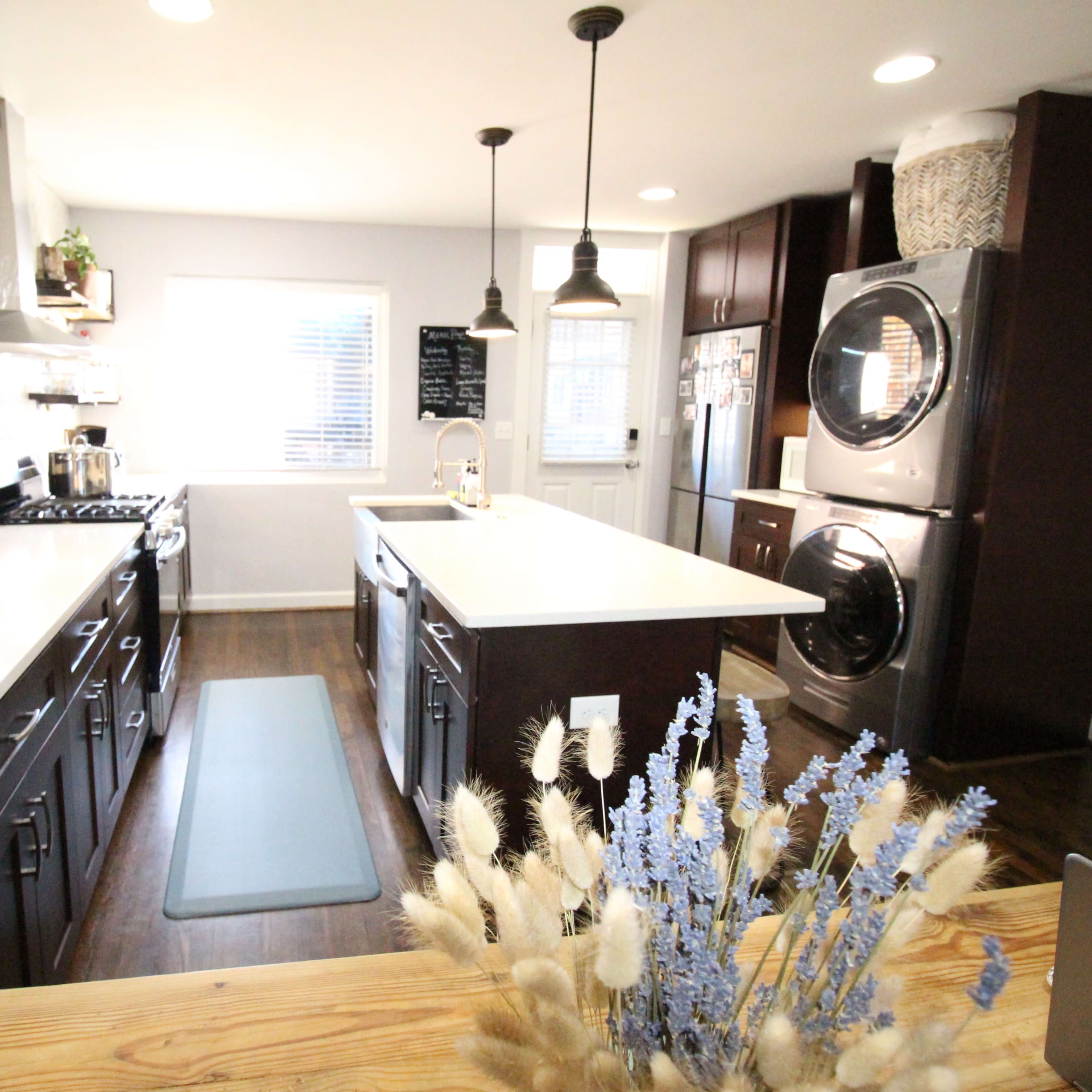 A modern kitchen featuring dark cabinets, a large island with a white countertop, and stainless steel appliances.