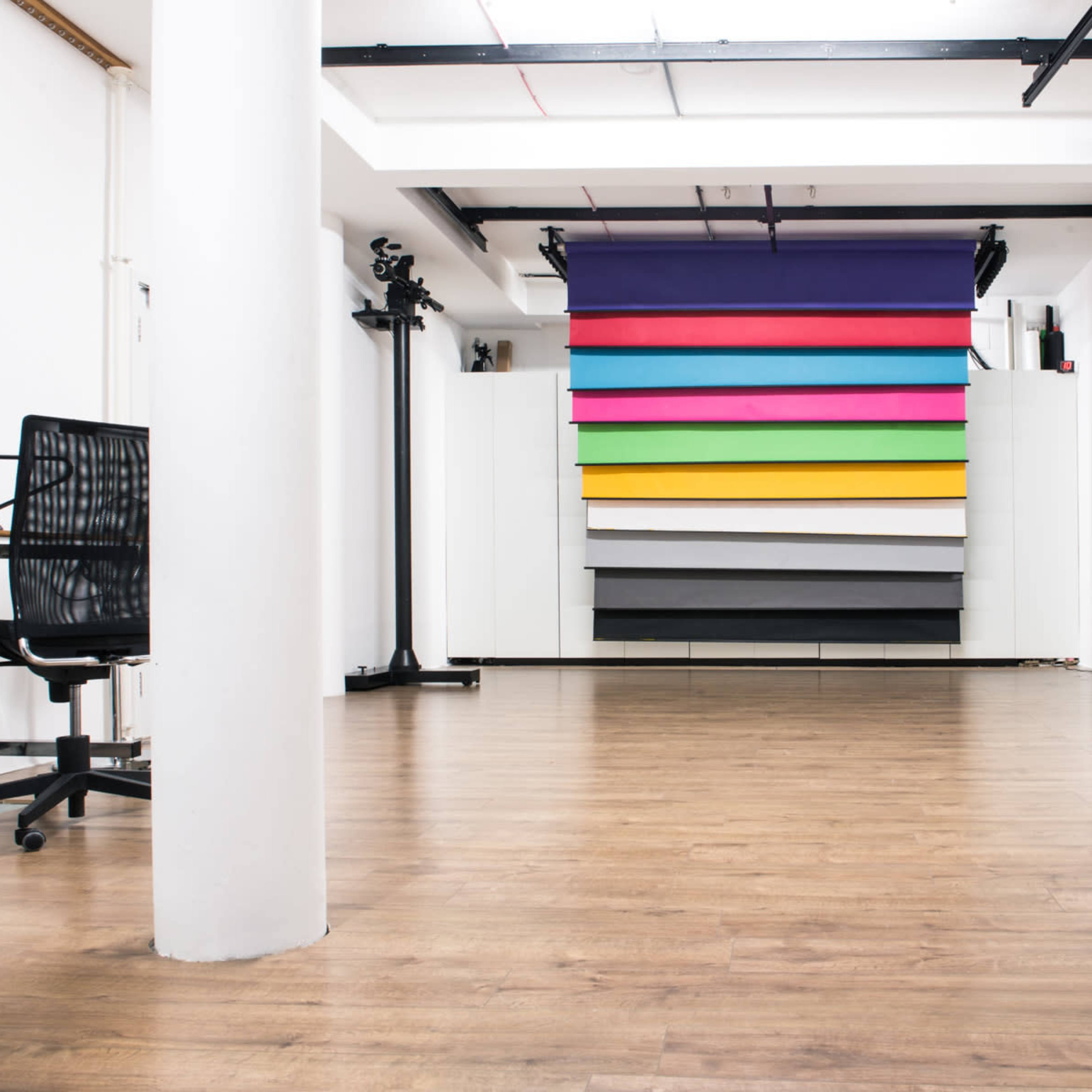 A spacious studio with a row of colorful backdrops, a black office chair, and a computer on a desk.
