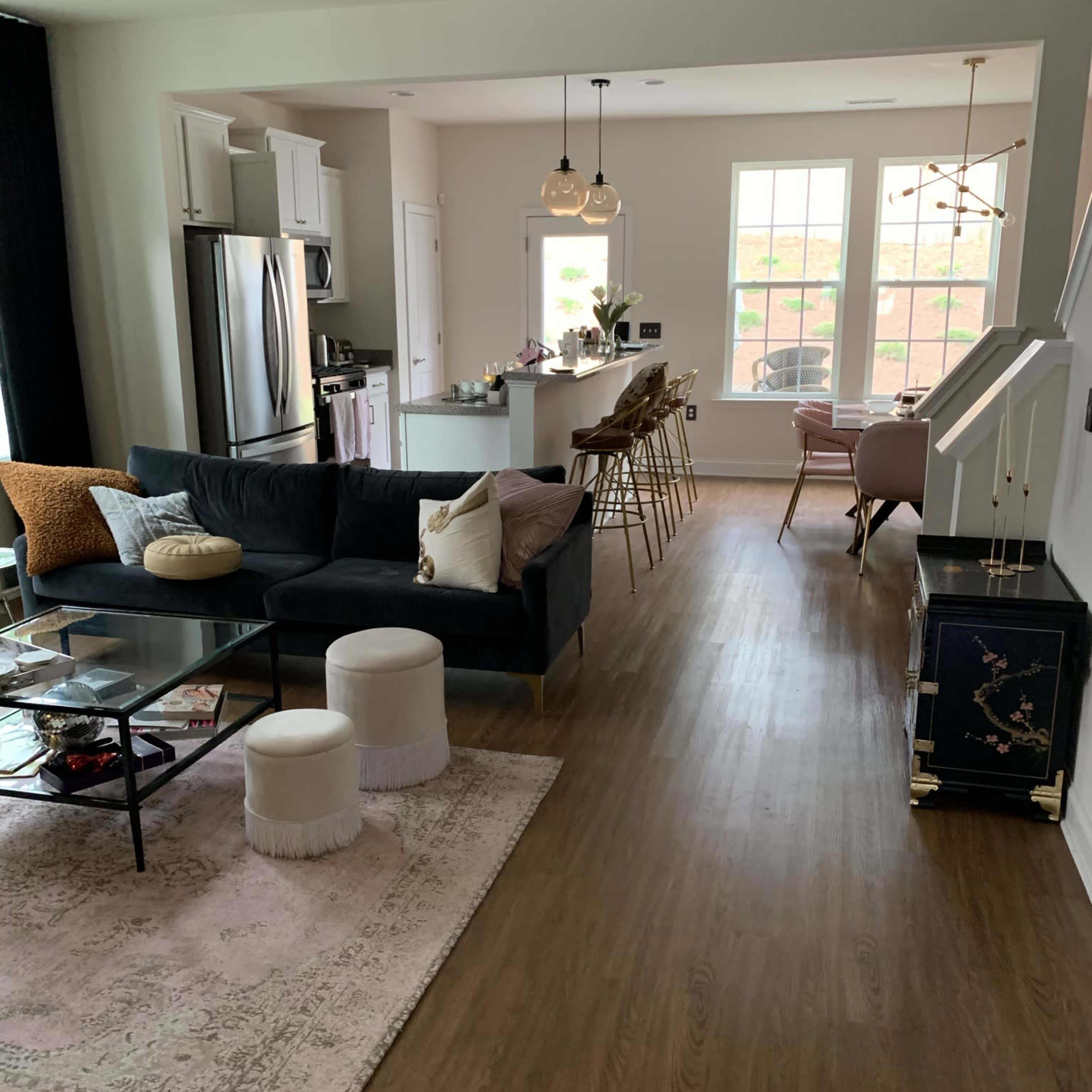 A modern open-concept living and dining area featuring a dark sofa, a glass coffee table, and a kitchen with bar stools.