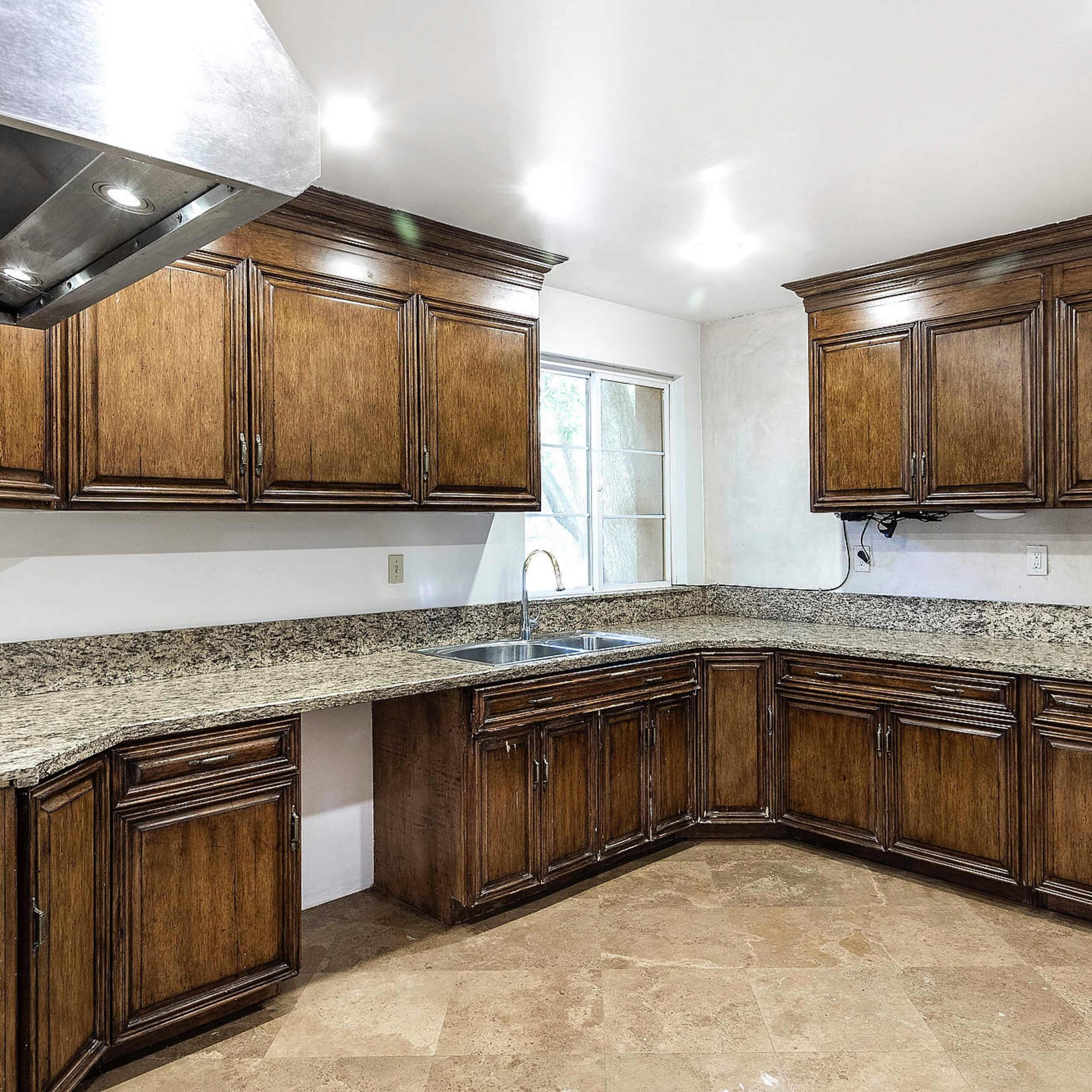 A kitchen with wooden cabinetry, a granite countertop, and a large window above the sink.