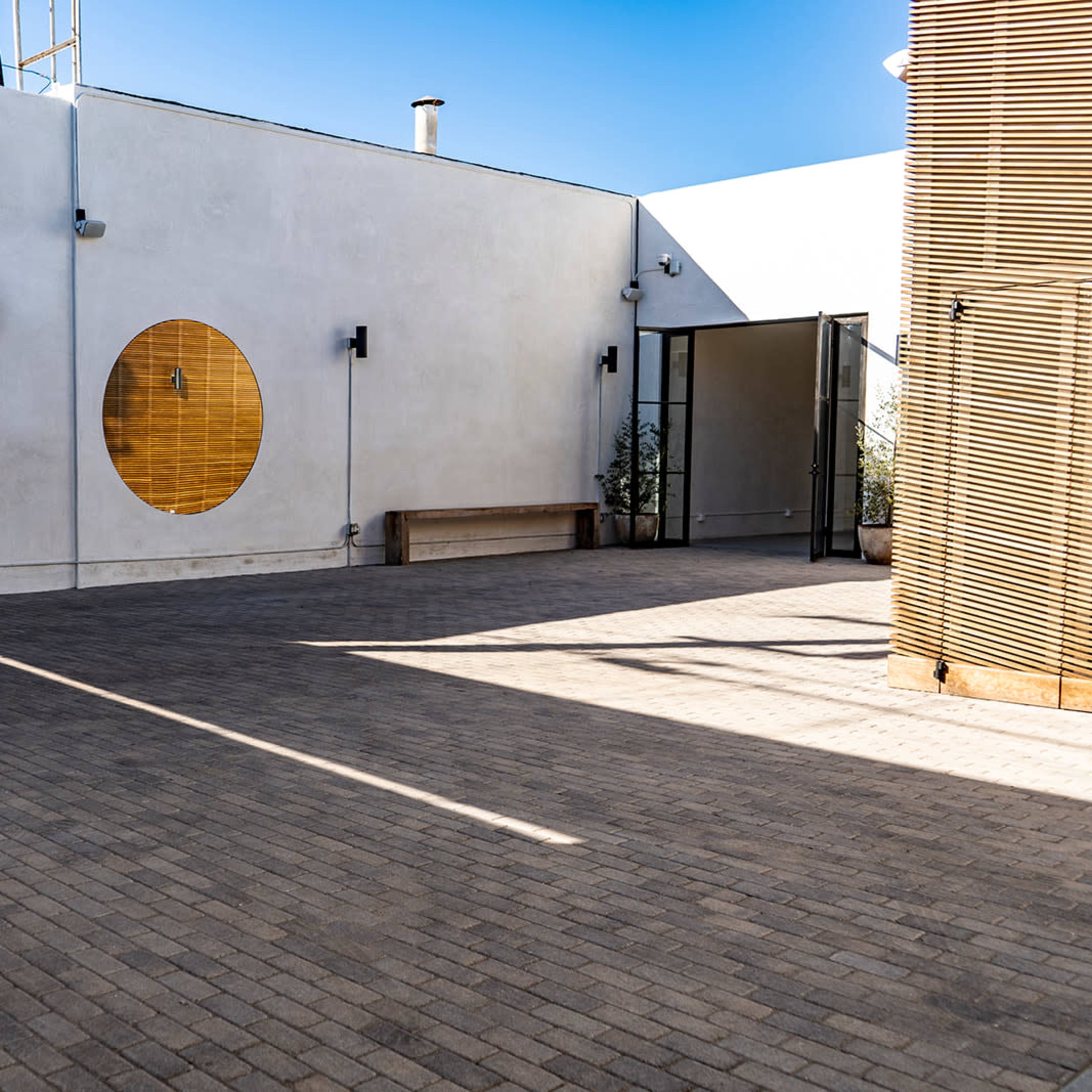 A spacious outdoor area with a textured stone surface, a large circular window on a white wall, and wooden elements along the perimeter.