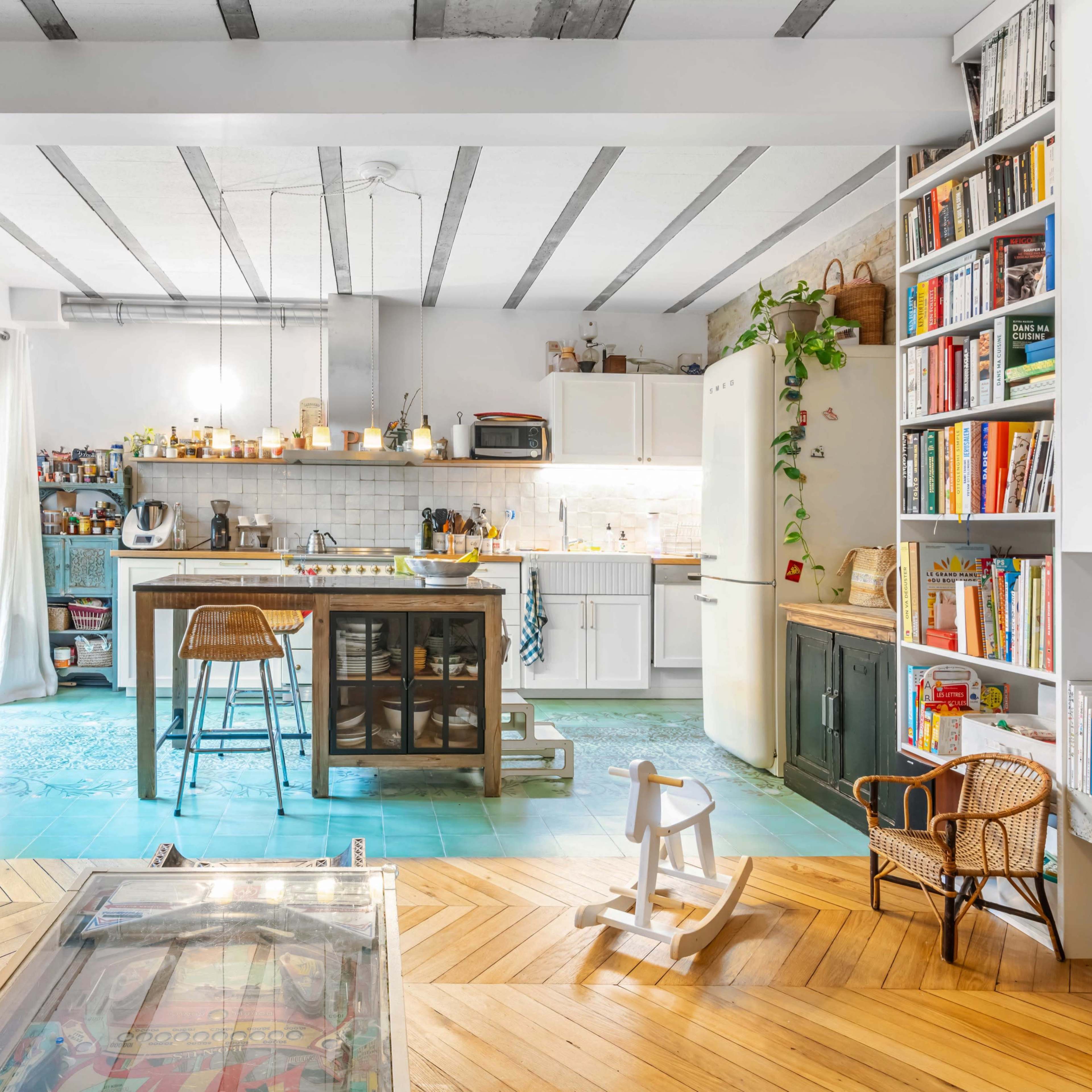 A cozy kitchen and living area with a large island, multiple bookshelves, and a mix of wooden and tiled flooring.