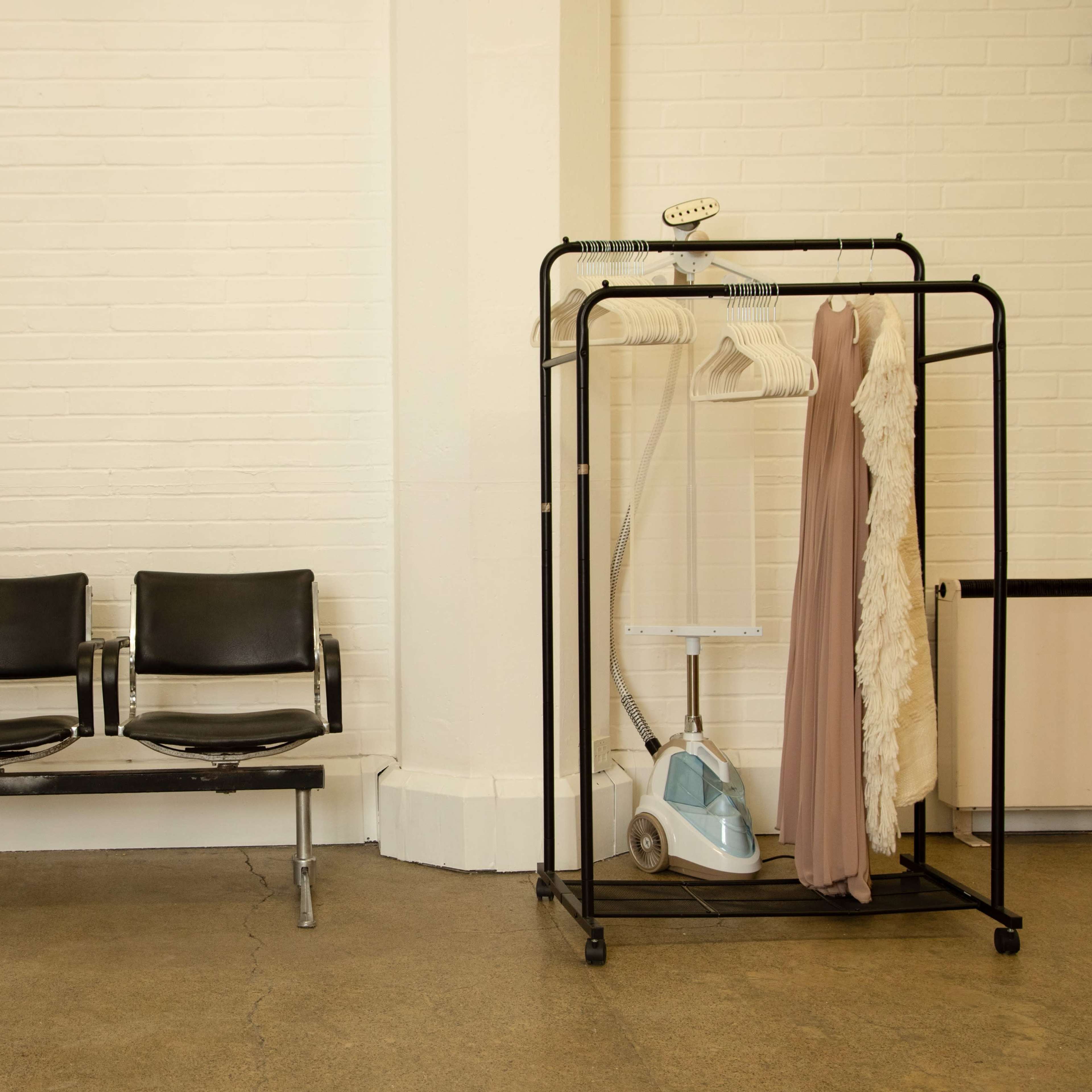 A row of three black seating chairs is positioned next to a clothing rack with a dress and a steamer.