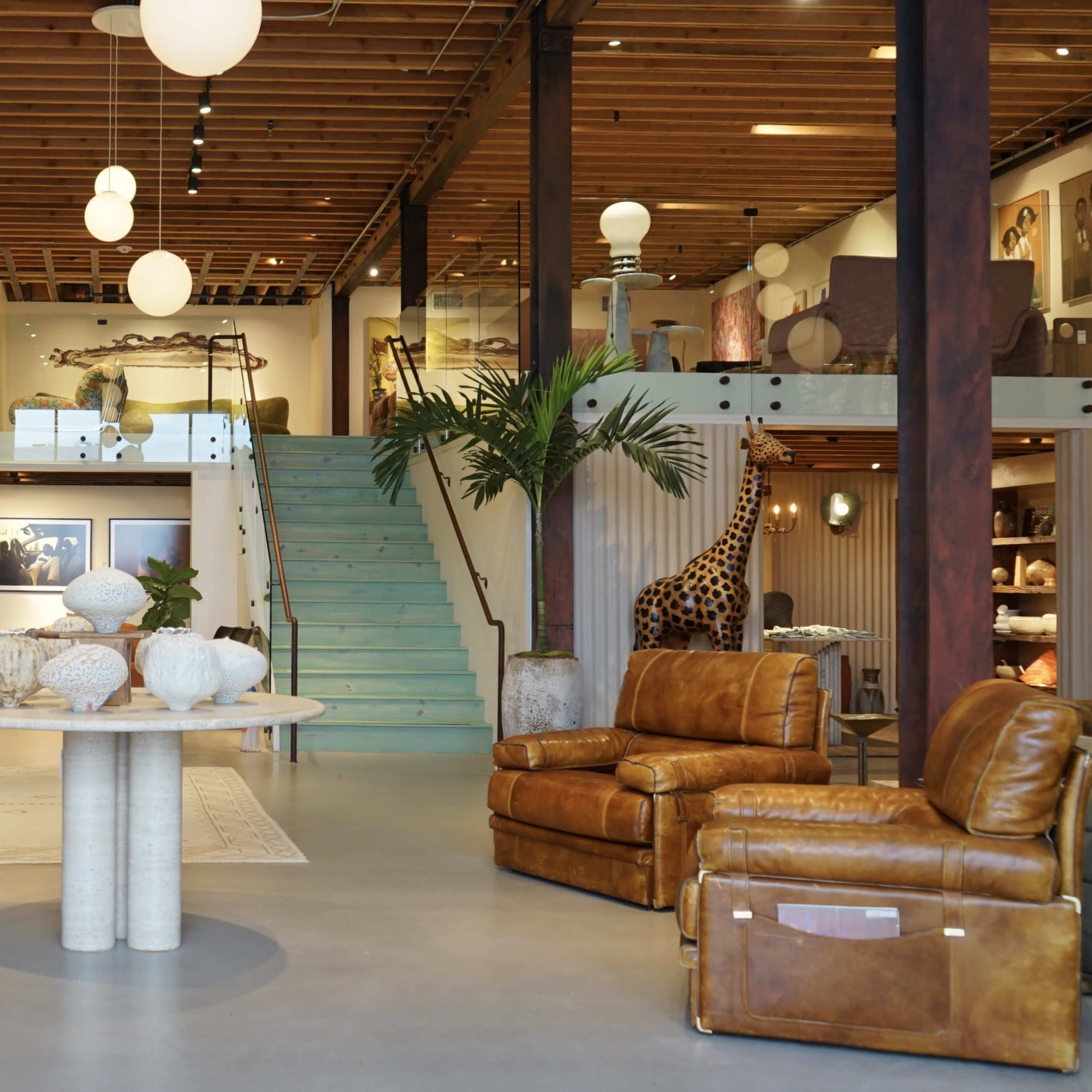 A spacious interior featuring modern furniture, a circular table with decorative vases, and a staircase leading to an upper level adorned with artwork.