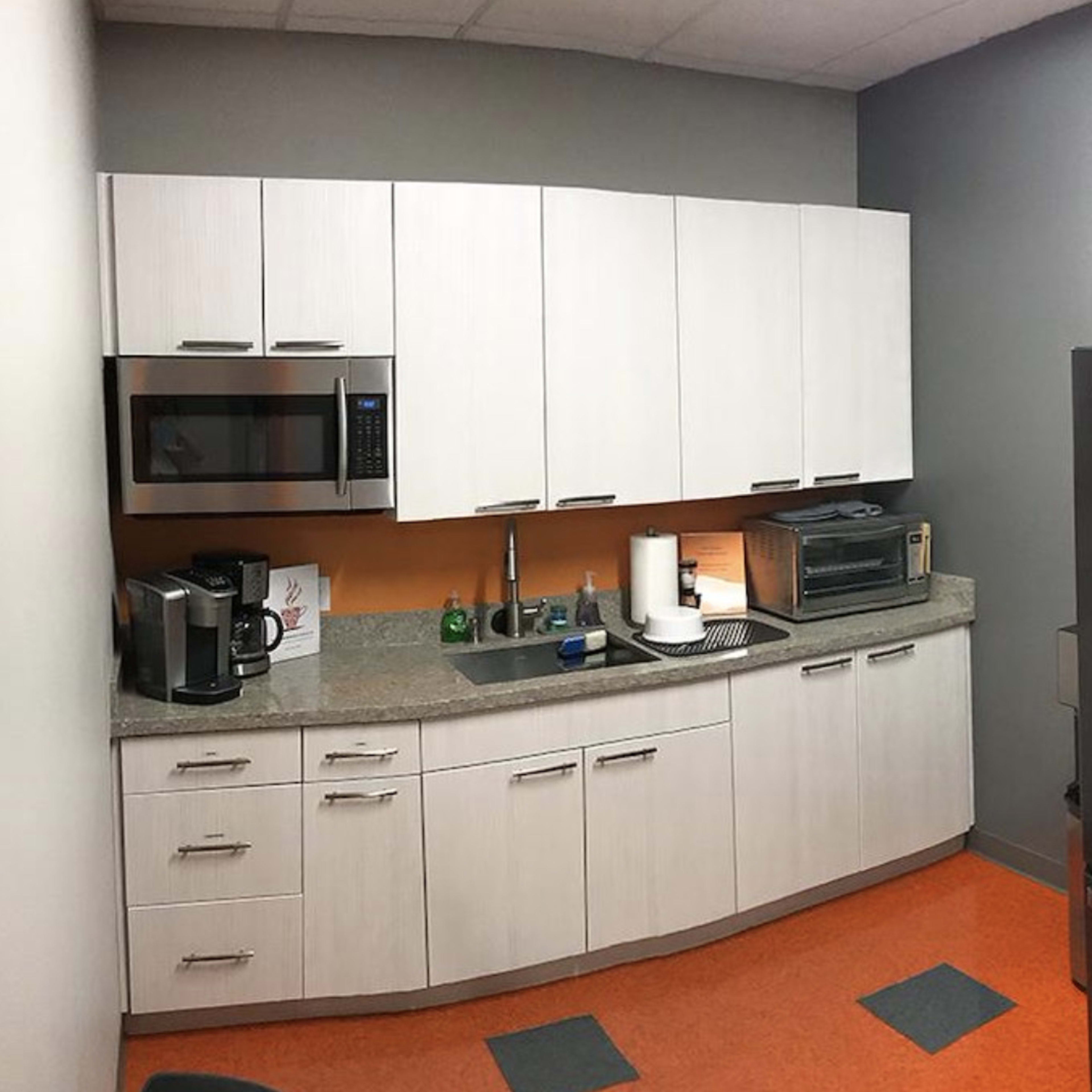 A kitchen features modern white cabinetry, a black refrigerator, a microwave, and a coffee machine against an orange wall.