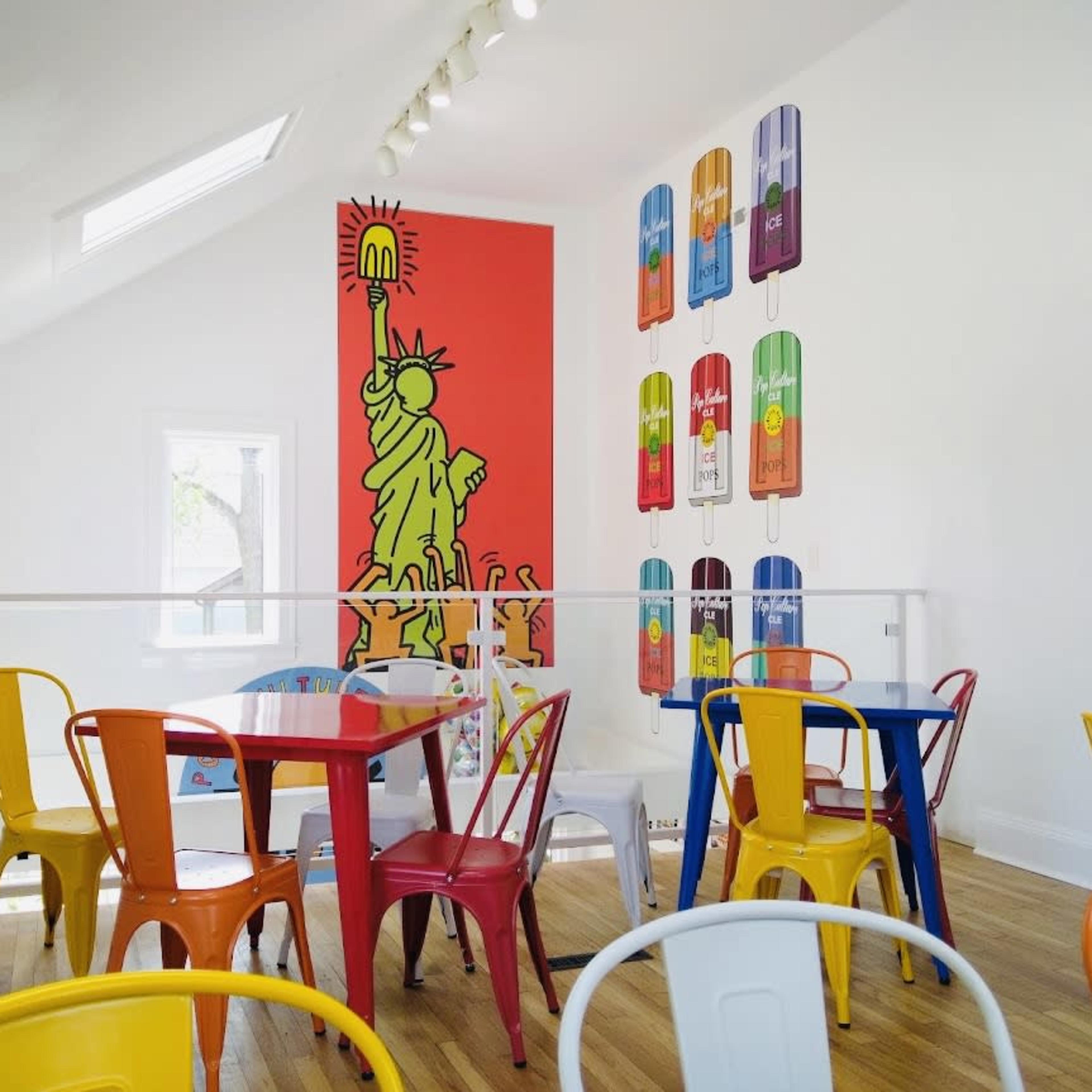 A brightly colored café interior with multicolored chairs and walls featuring graphic artwork, including a depiction of the Statue of Liberty.