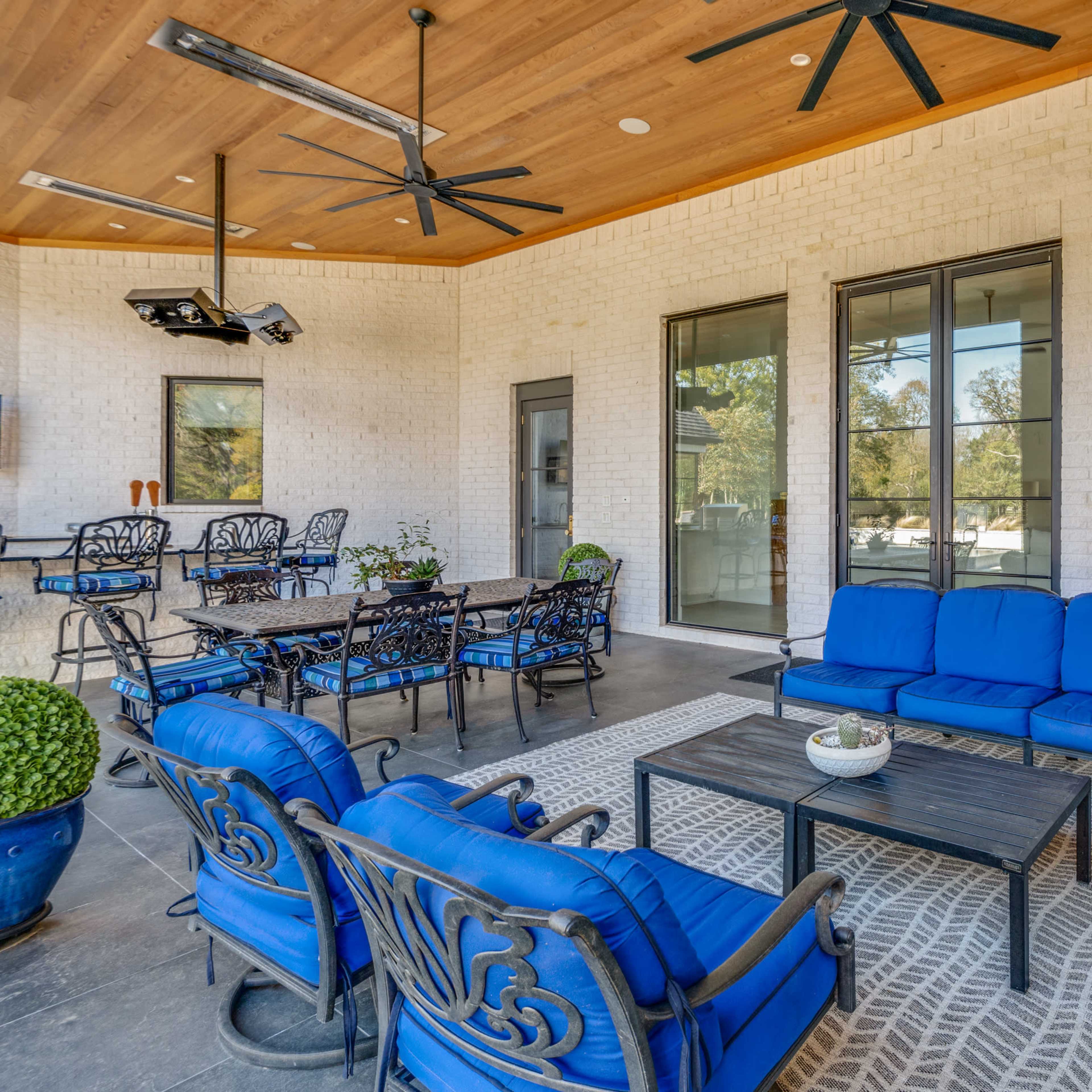 A covered outdoor living area featuring blue seating, a coffee table, and large glass doors opening to a pool view.