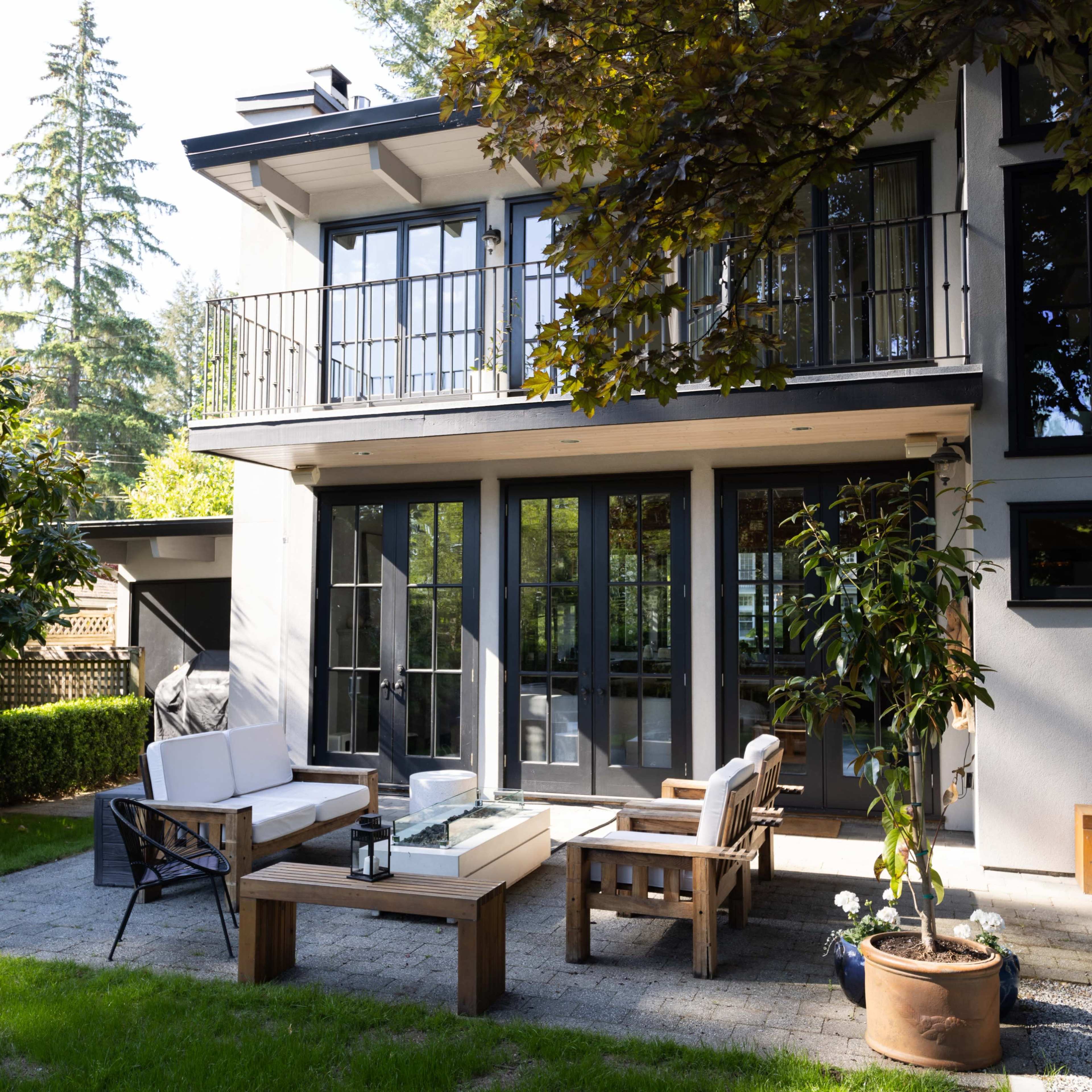 A modern home features a patio area with outdoor furniture, surrounded by greenery and trees.