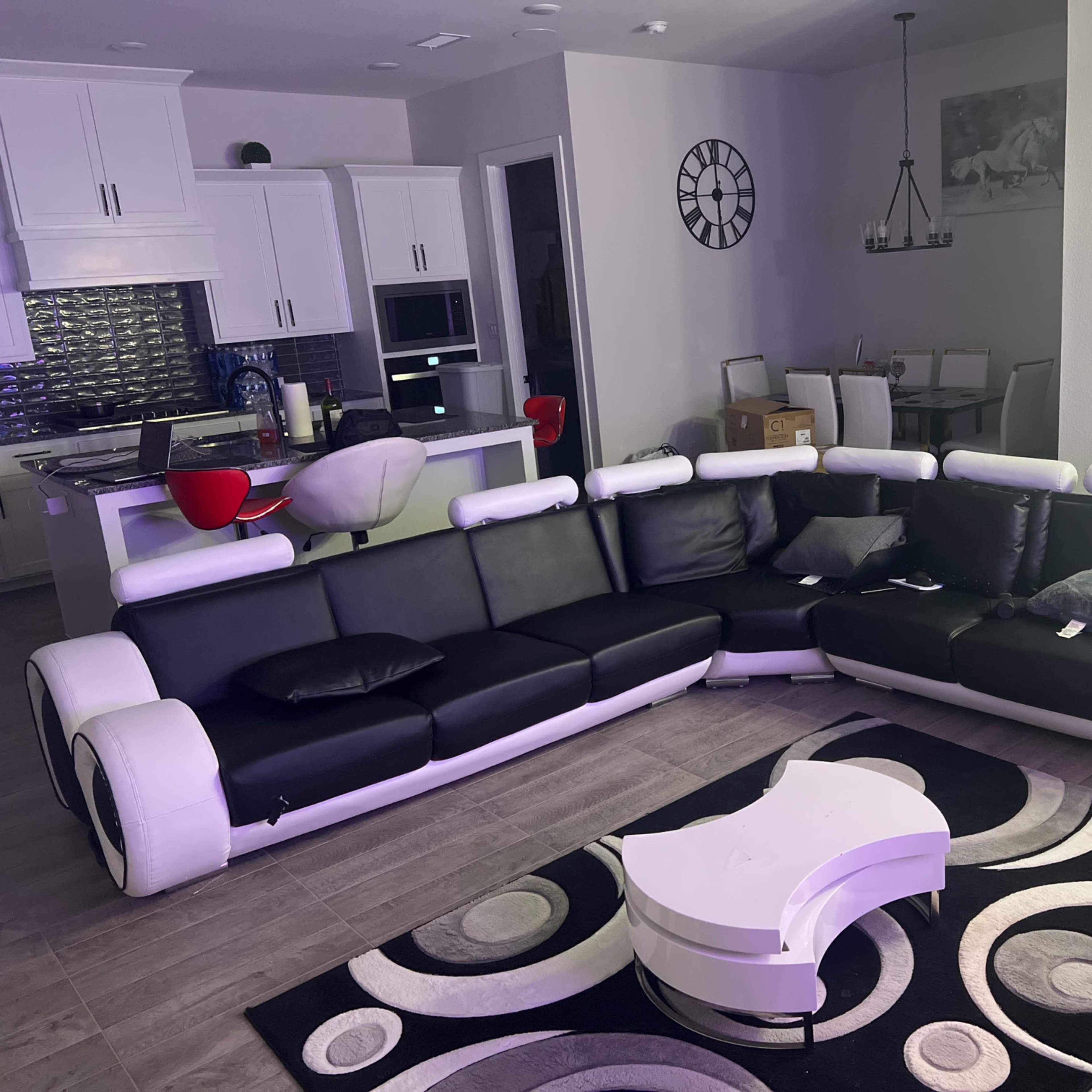 A modern living room with a black and white sectional sofa, a round coffee table, and a kitchen area in the background.