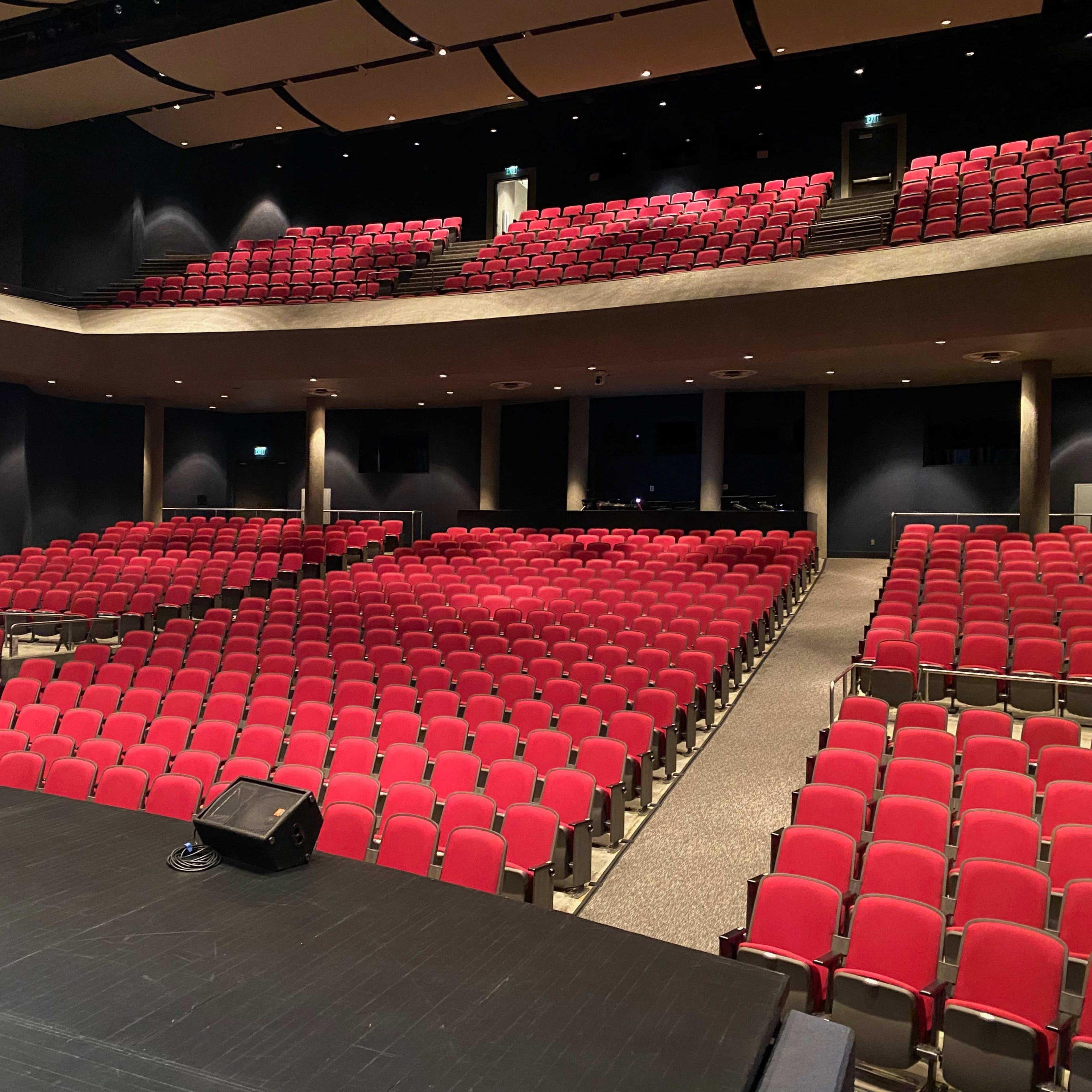 A theater auditorium with rows of red seating arranged in a semi-circular layout from a stage perspective.