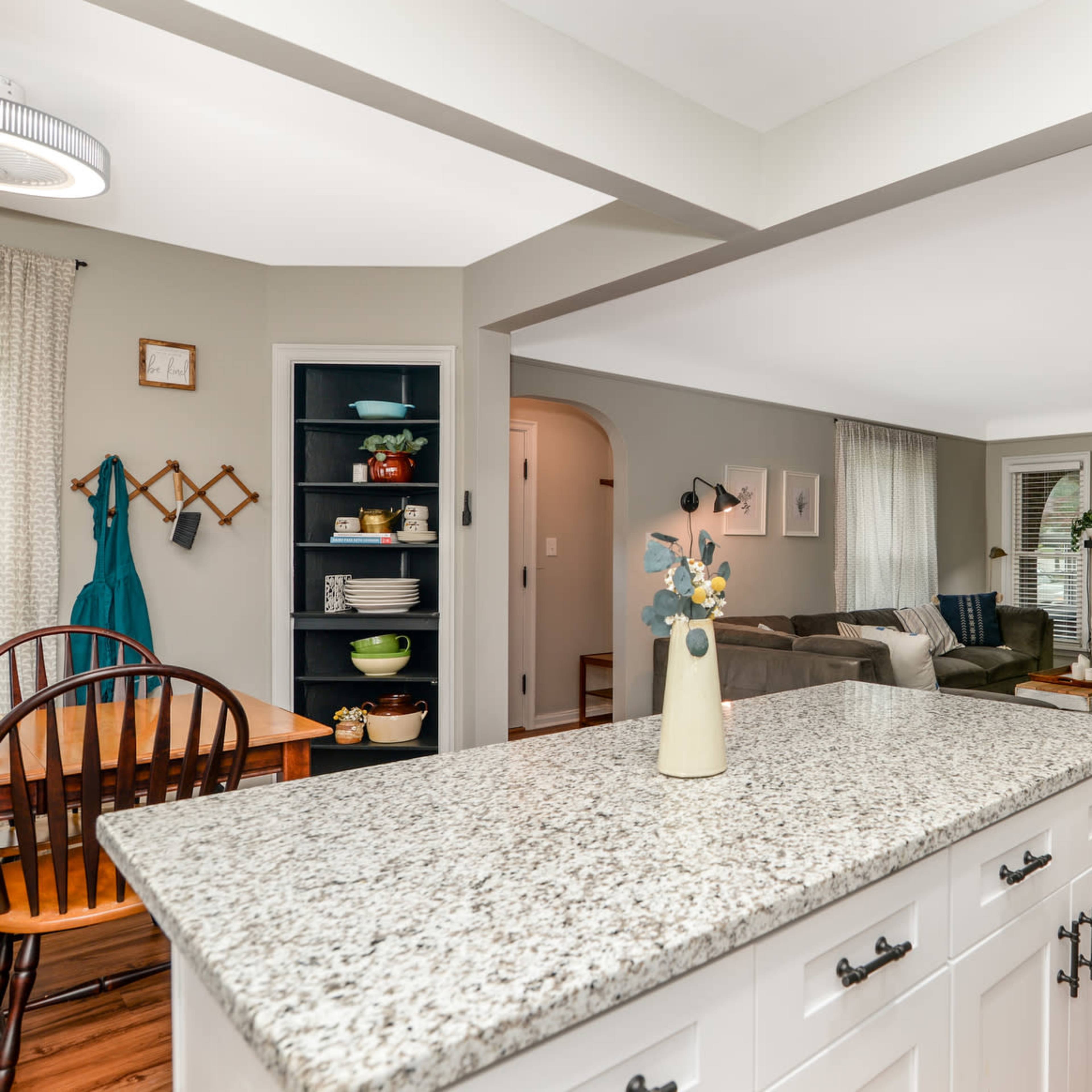 A kitchen with a granite countertop facing an open living area featuring a fireplace and seating.