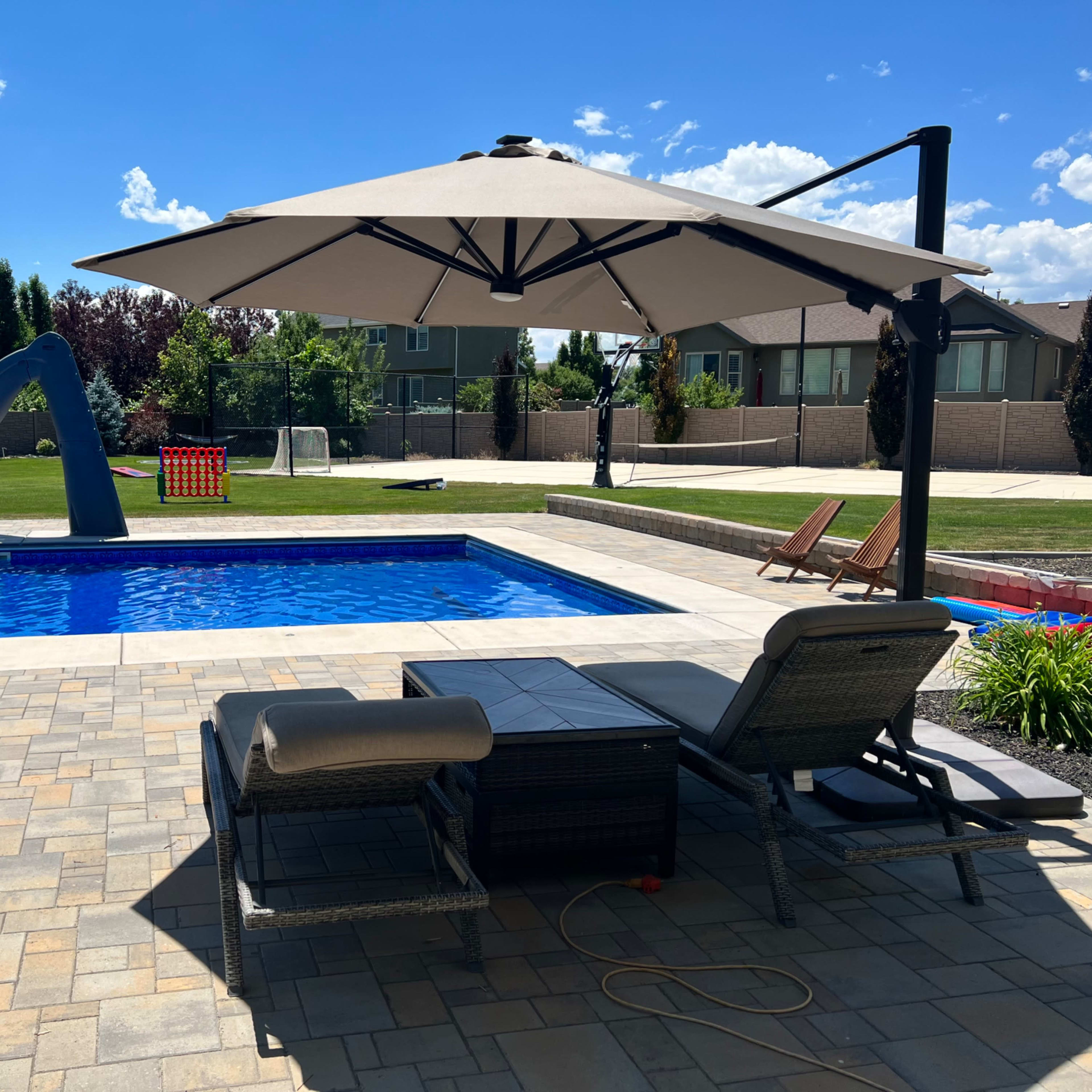 A backyard pool area featuring a blue water slide, a shaded seating area, and lounge chairs beside a clear swimming pool.