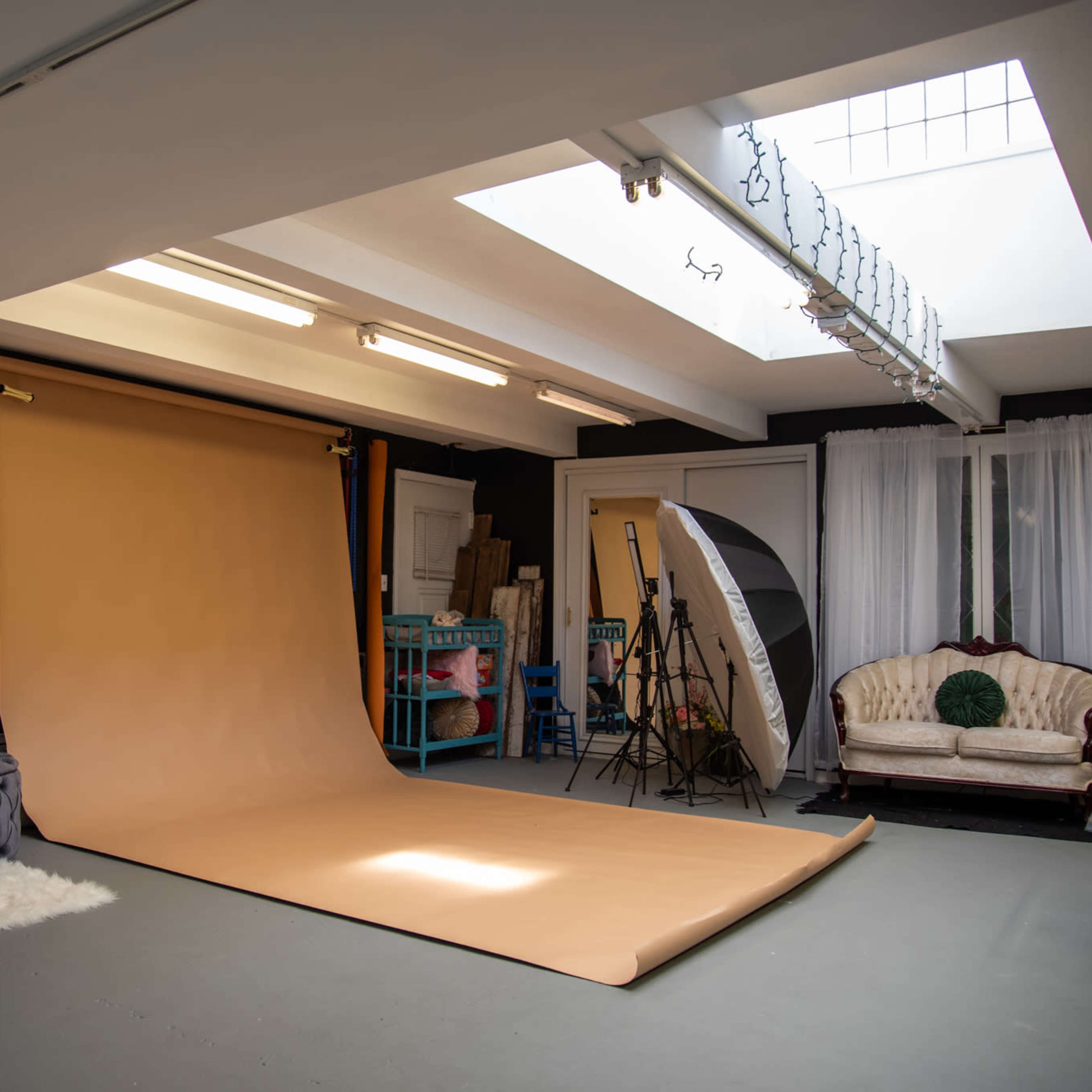 A photography studio featuring a large beige backdrop, soft lighting equipment, and vintage furniture in a well-lit room.