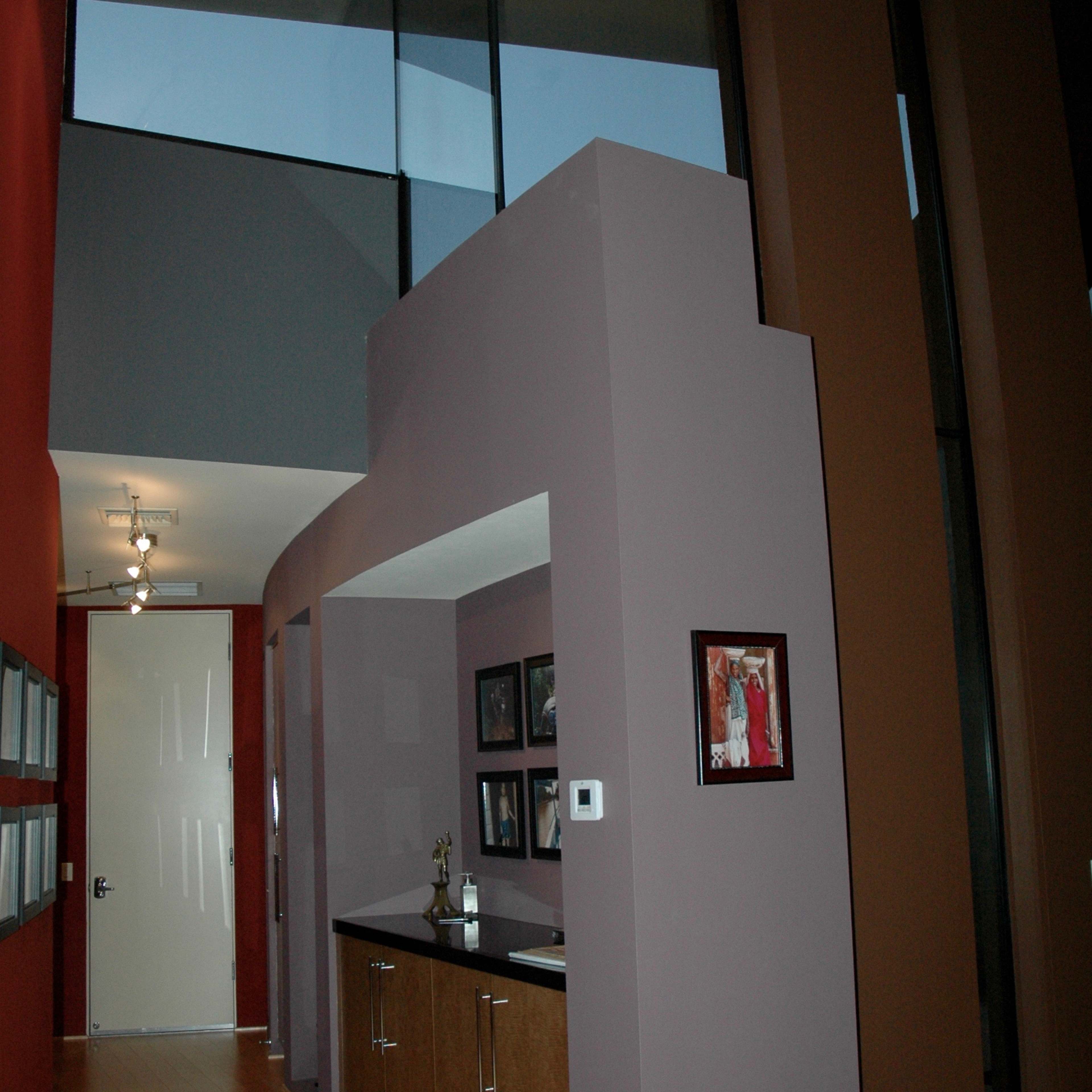 A modern entryway with a high ceiling, featuring a purple partition and wooden cabinetry along one wall, framed photographs on display, and a door leading to another space.