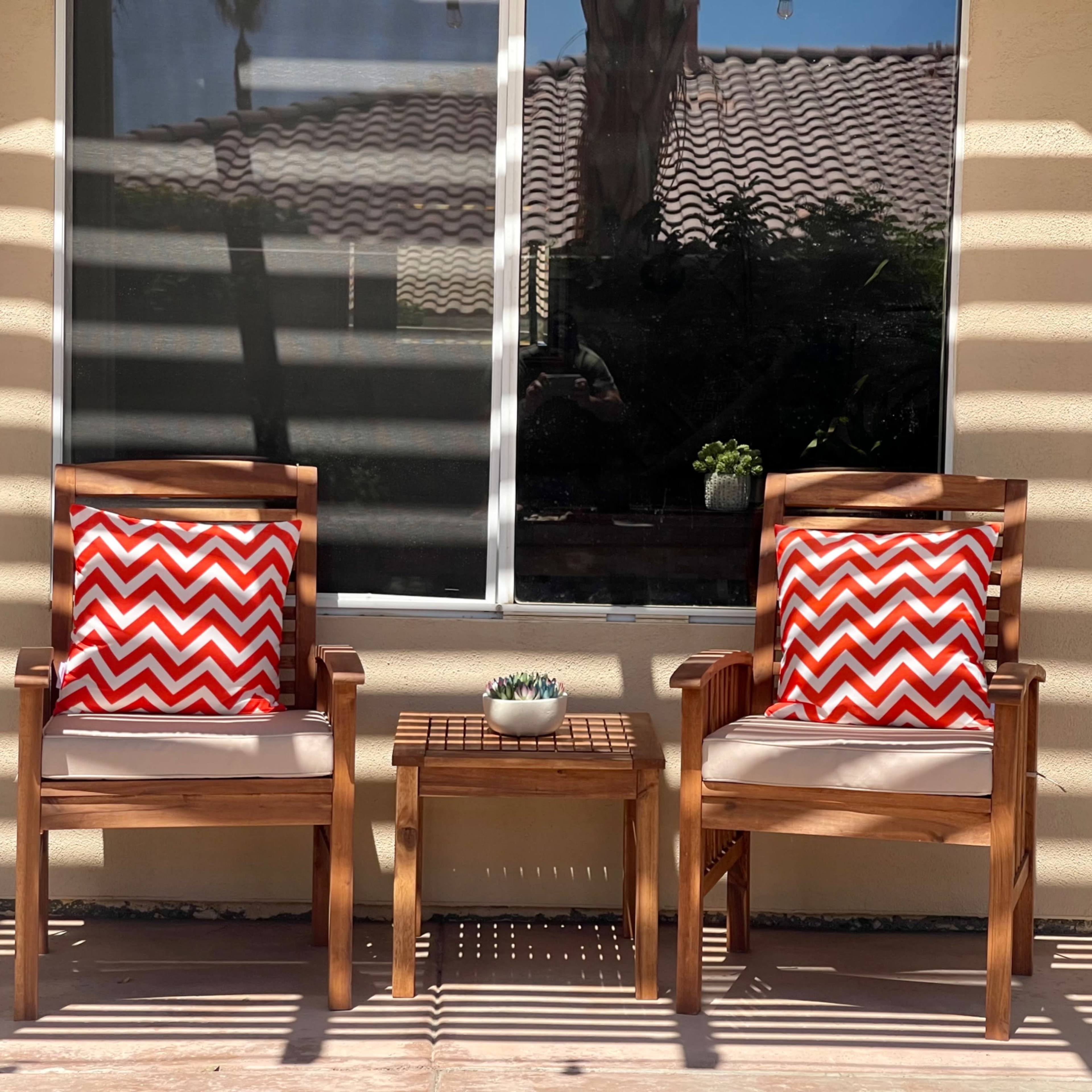 Two wooden chairs with red and white chevron-patterned cushions are positioned beside a small table in front of a window, with sunlight casting striped shadows across the scene.
