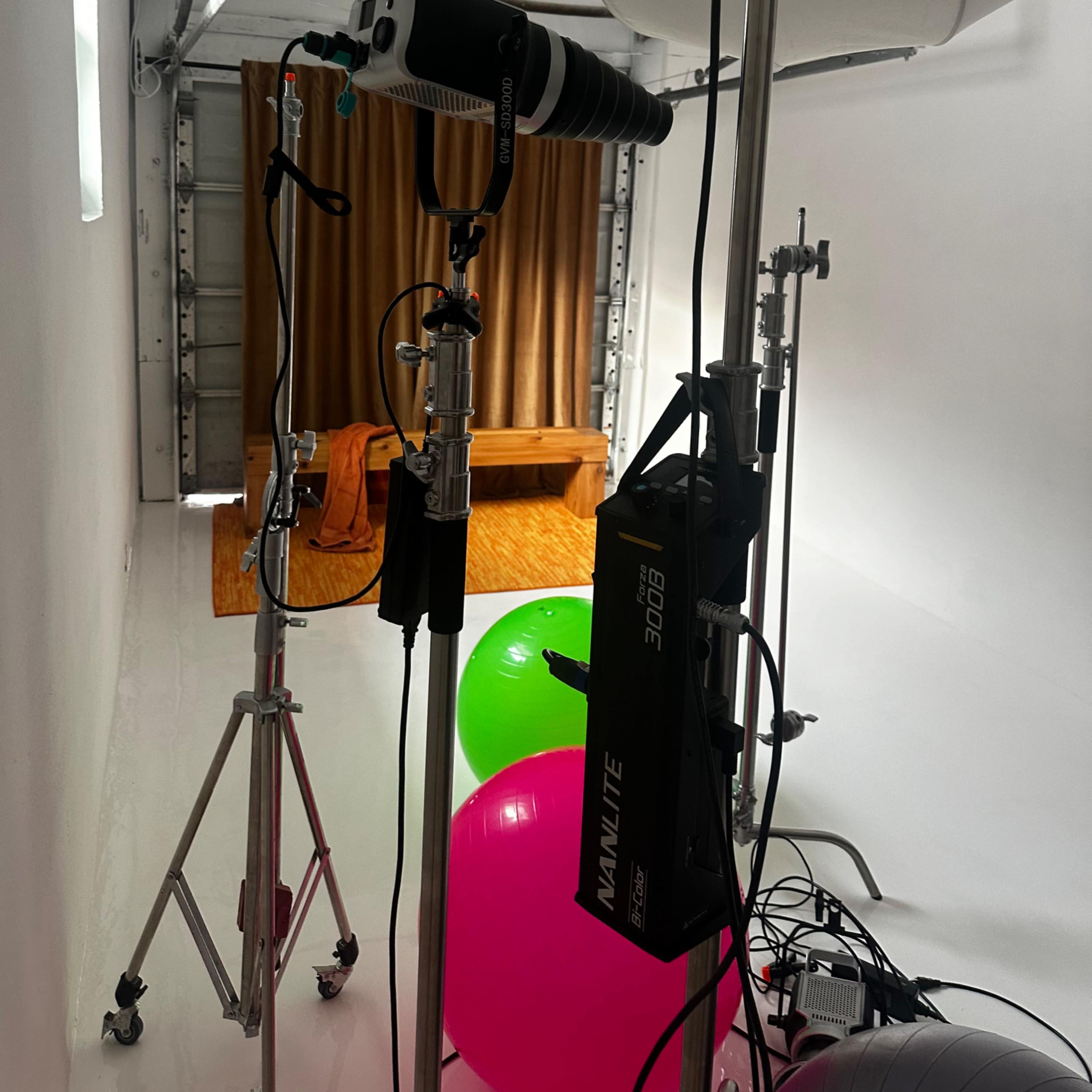 A photography studio setup with lighting equipment, a backdrop of brown curtains, and colorful balloons on the floor.
