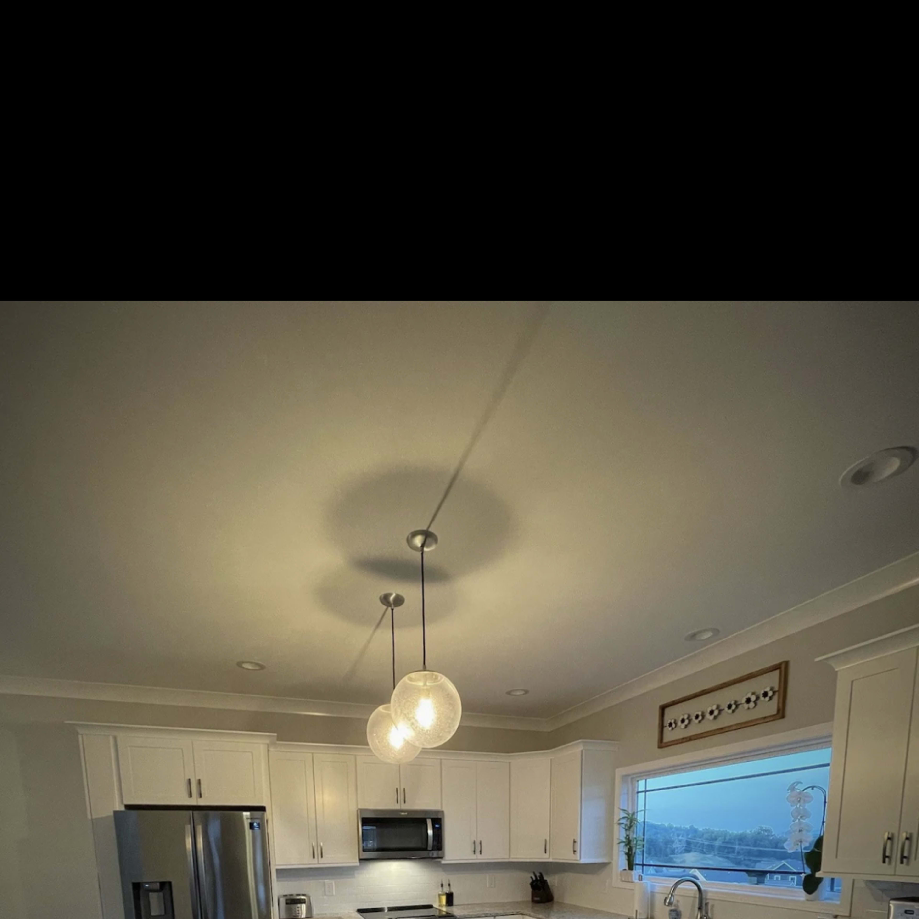 A modern kitchen with white cabinetry, a central island with seating, and large windows overlooking a scenic view.