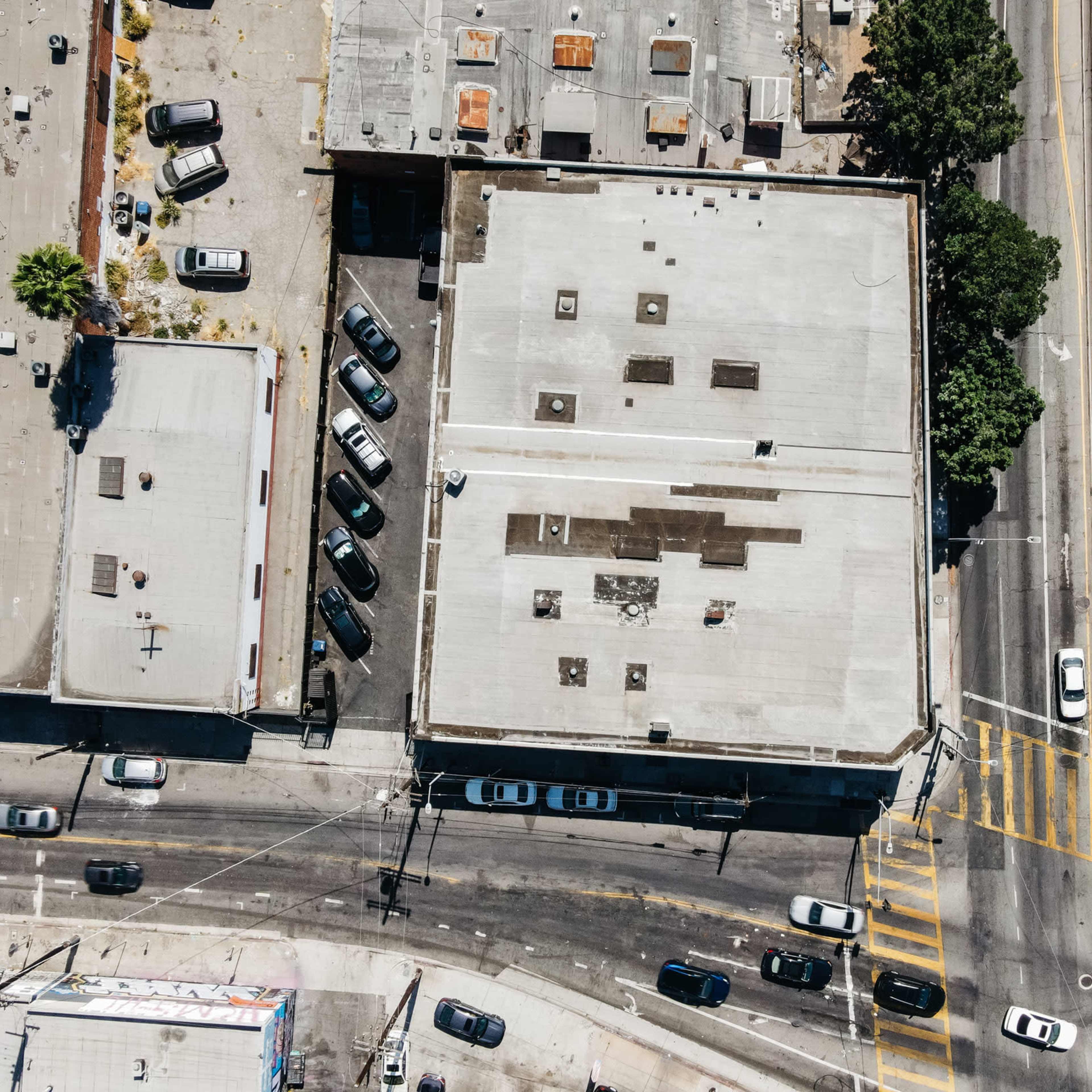 An aerial view shows a city block with several flat-roofed buildings and vehicles on the surrounding streets.
