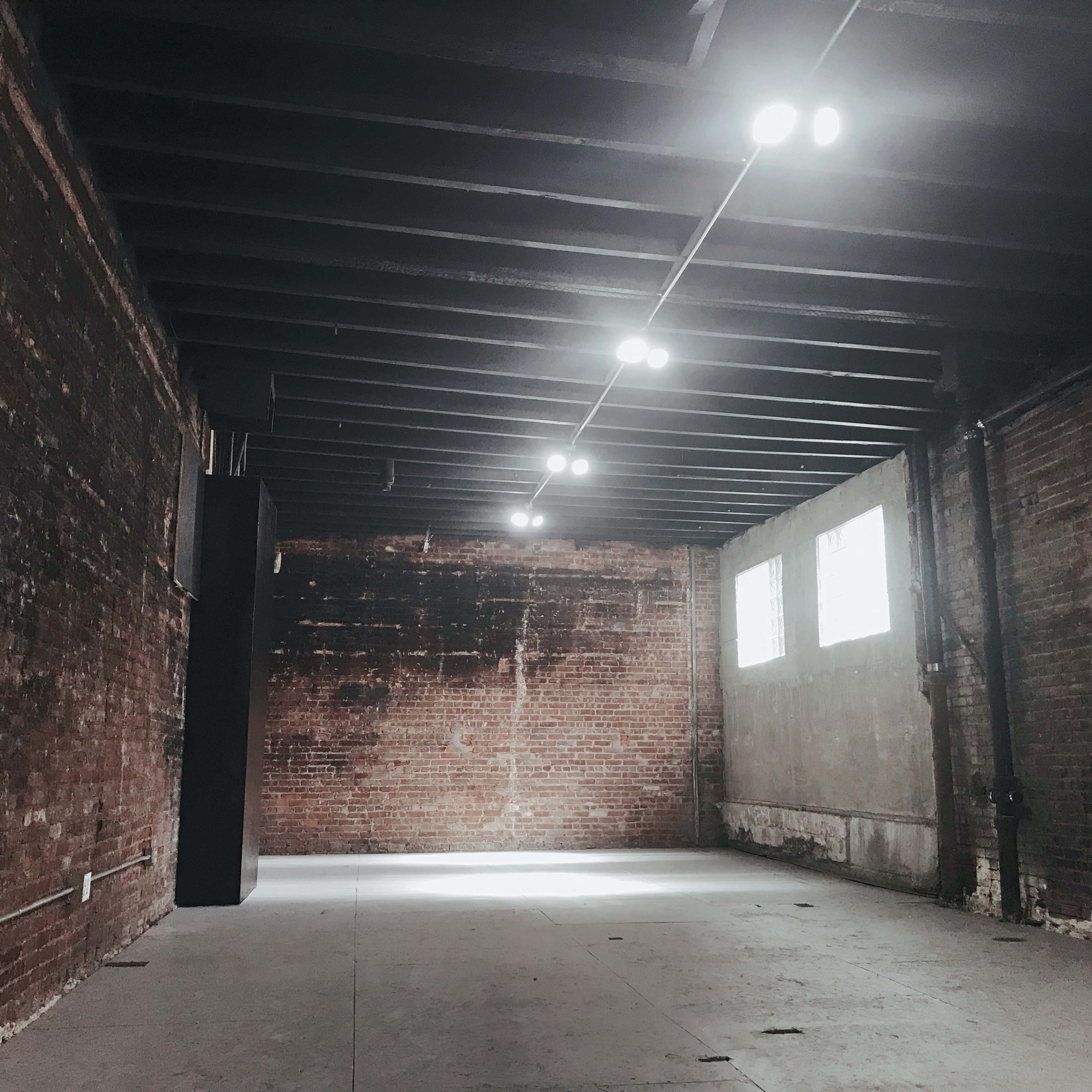 An empty room with exposed brick walls and overhead track lighting.