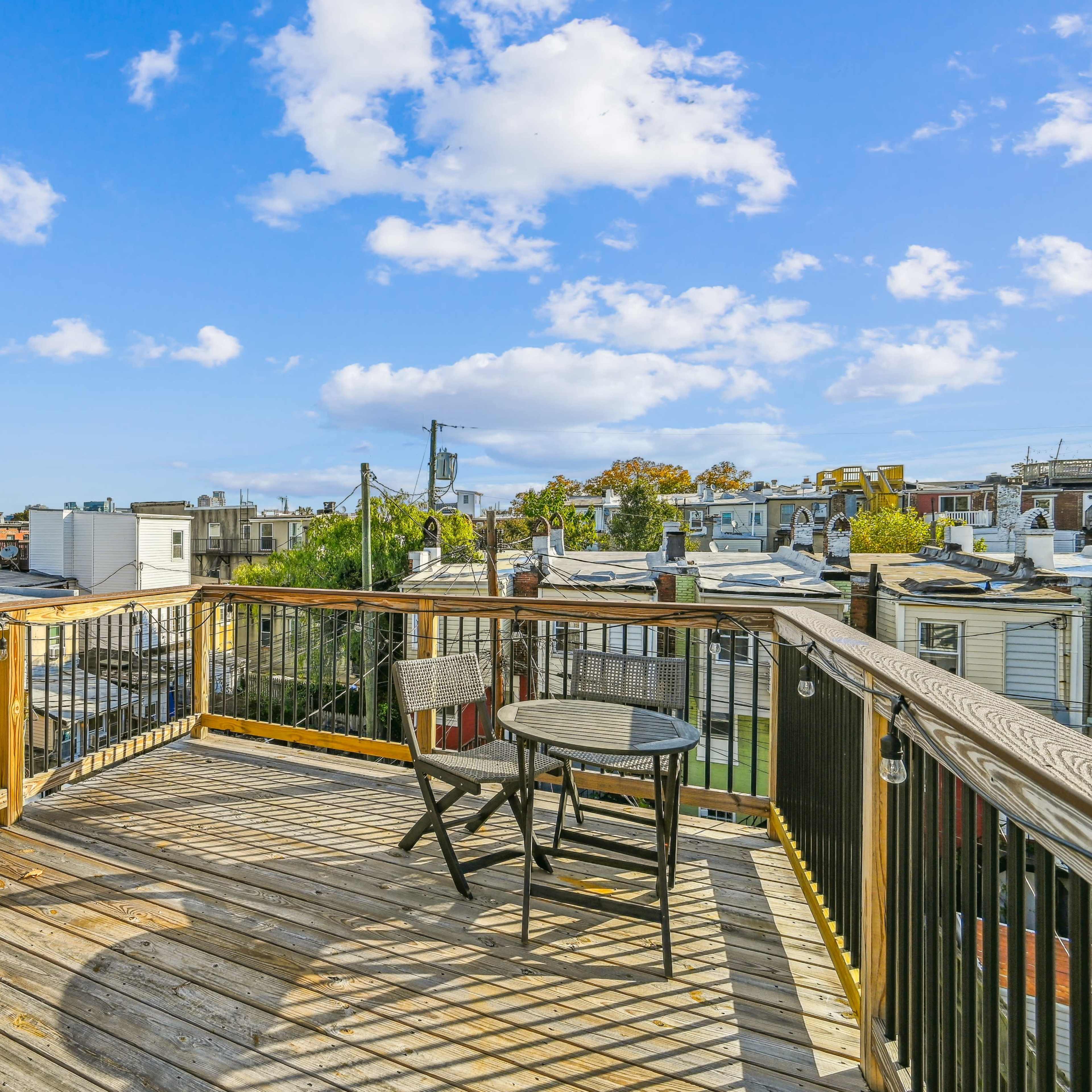 A wooden deck with two chairs overlooks a cityscape under a blue sky with scattered clouds.