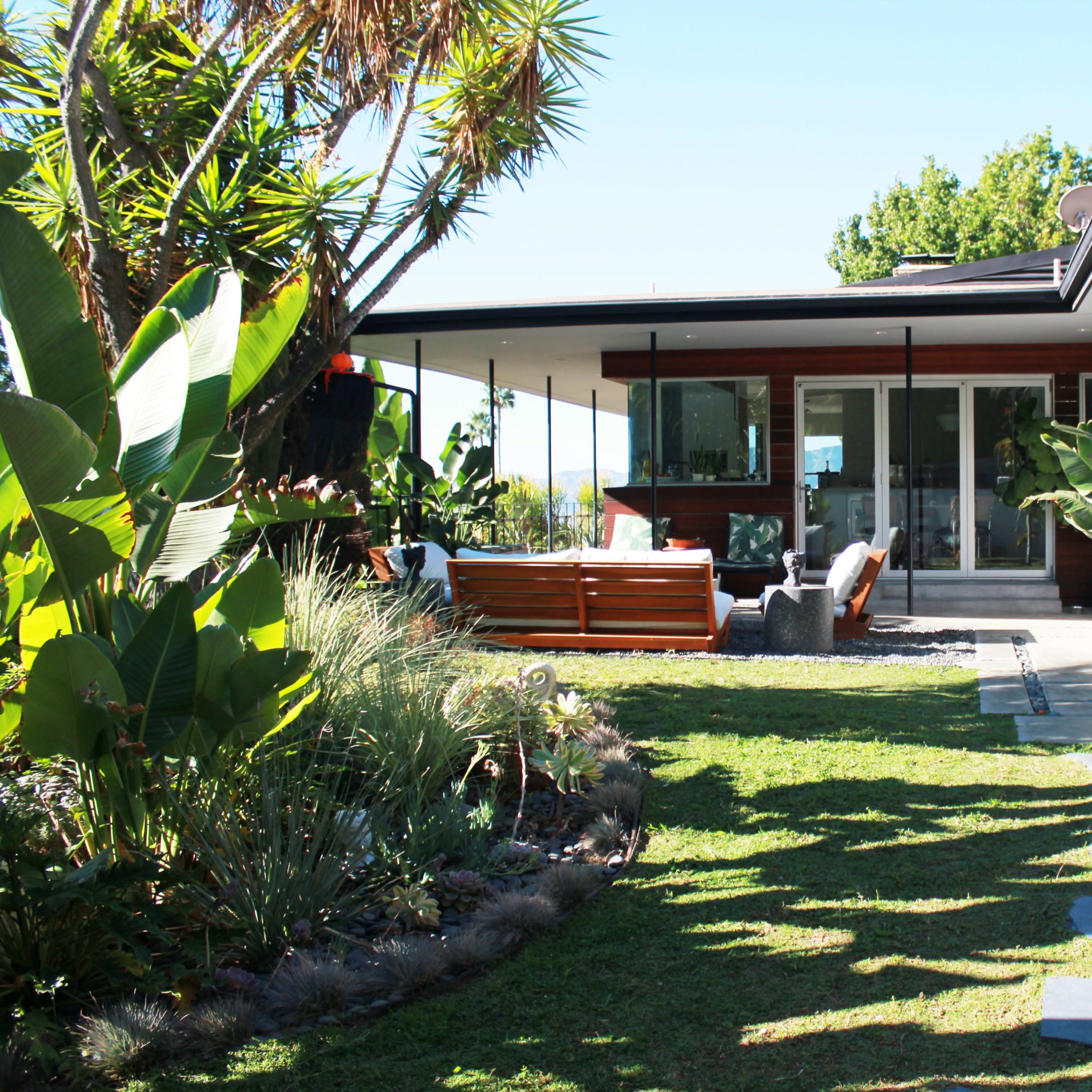 A pathway of stones leads through a landscaped yard to a modern house with large glass doors and a deck.