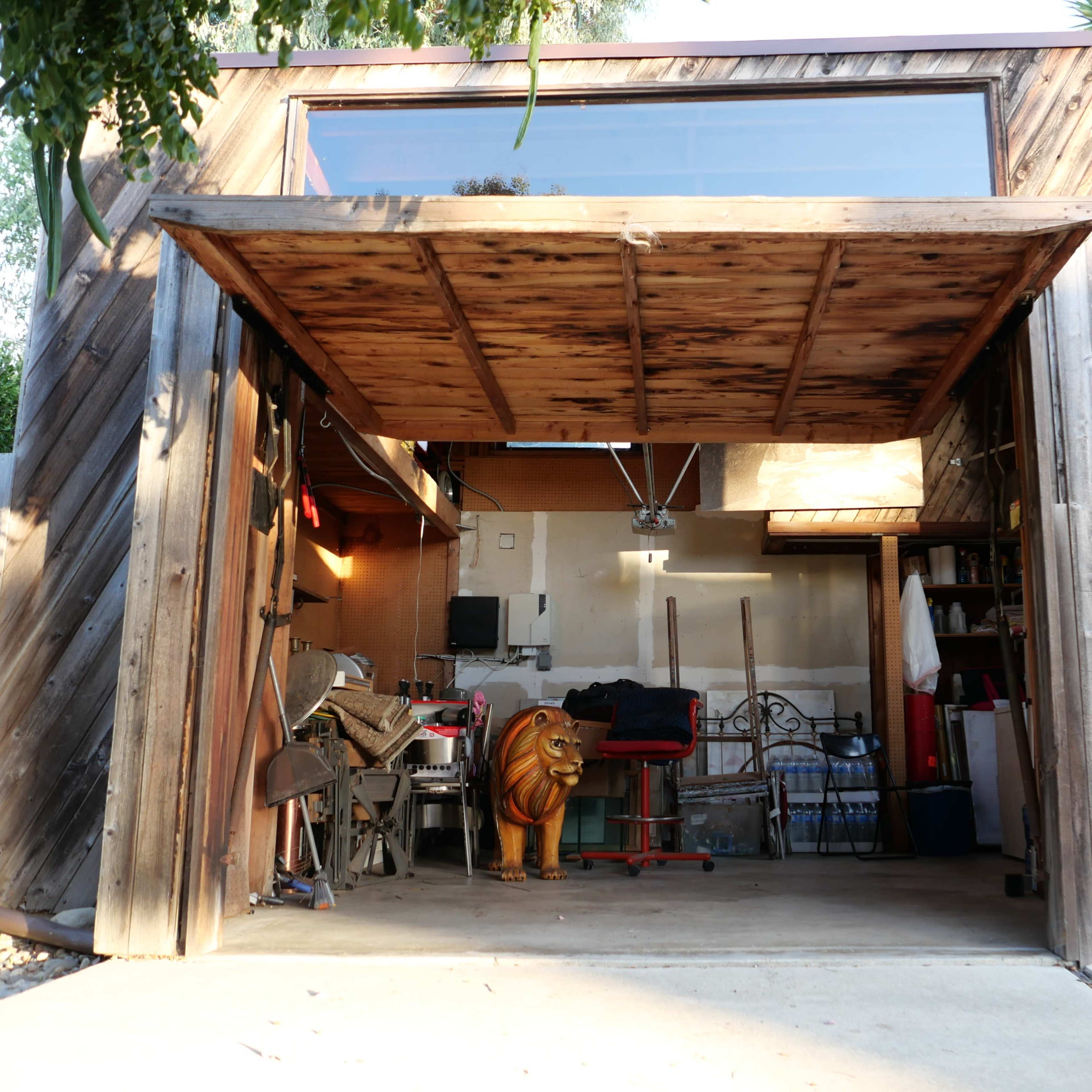 A wooden garage with an open door reveals various tools and furniture inside, including a decorative lion statue.