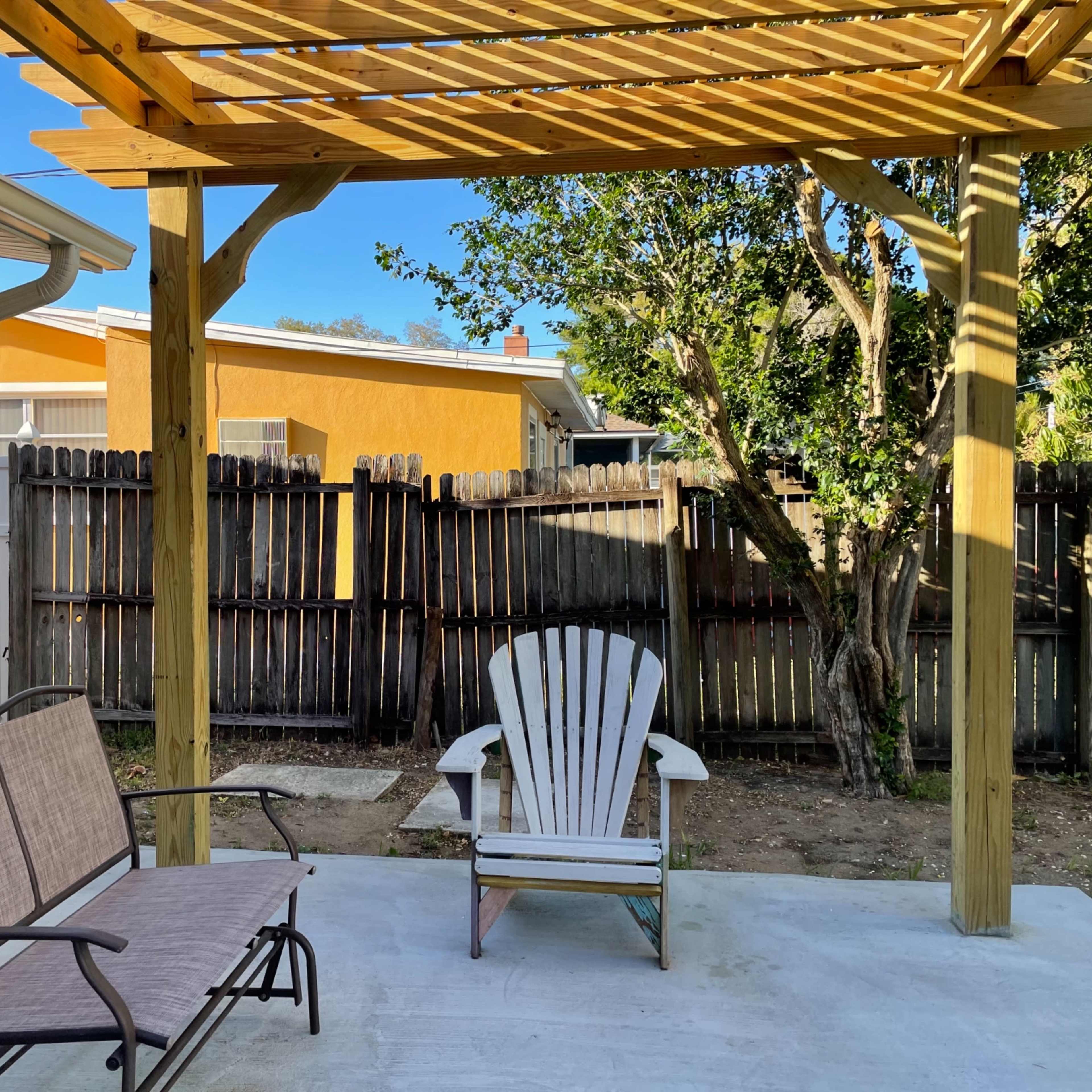 A covered patio features two chairs and overlooks a fenced yard with a wooden fence and nearby houses.